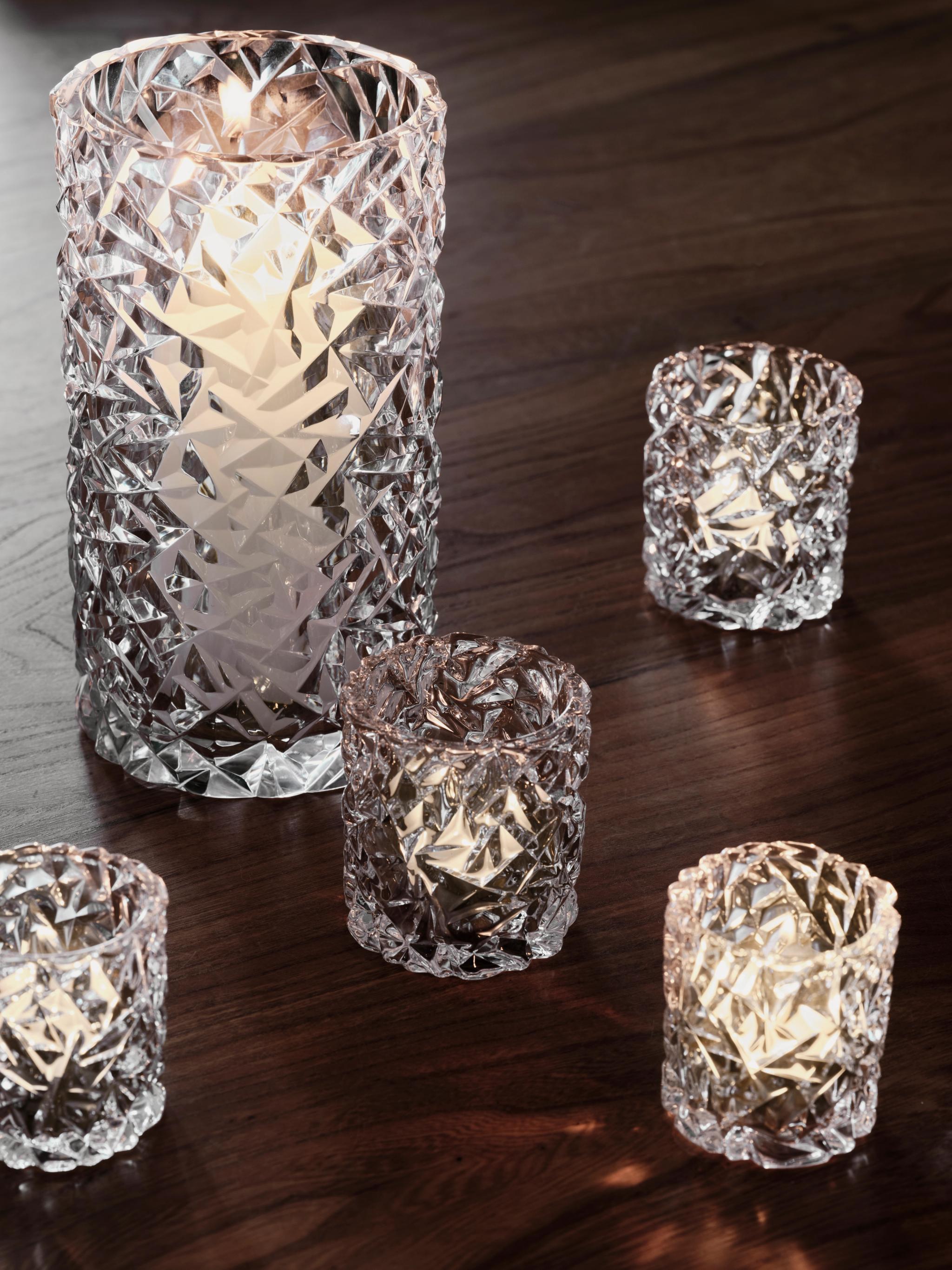 One tall and four small diamond-patterned glass votive holders with lit candles on a dark wooden table.