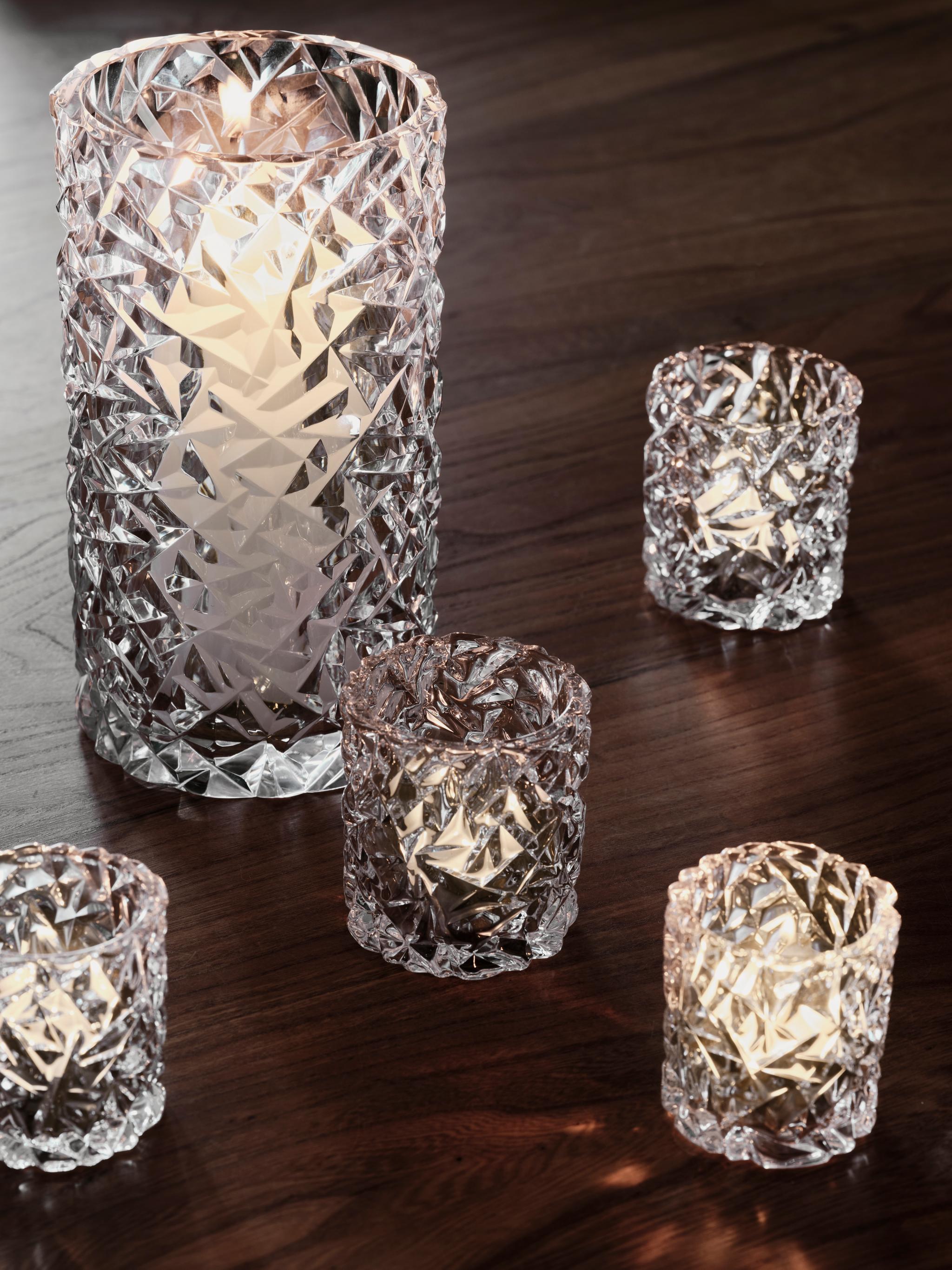 One tall and four small diamond-patterned glass votive holders with lit candles on a dark wooden table.