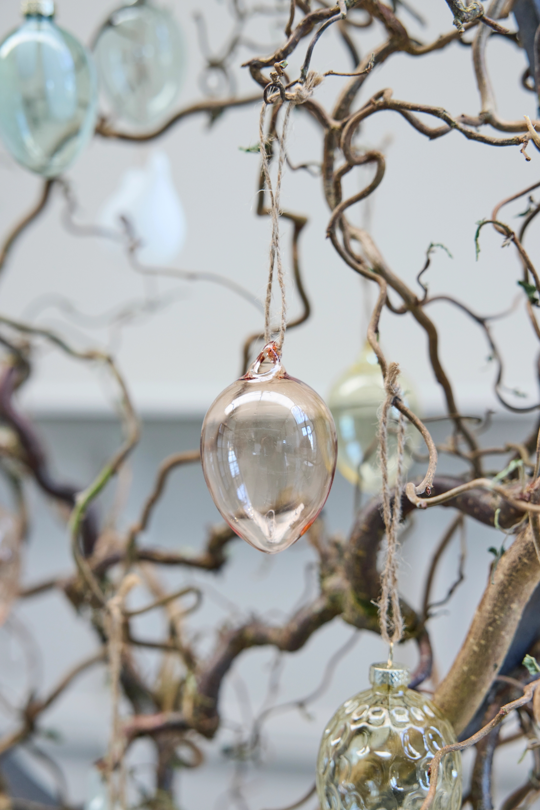 Klare og ravfargede glassornamenter som henger fra vridde grener.