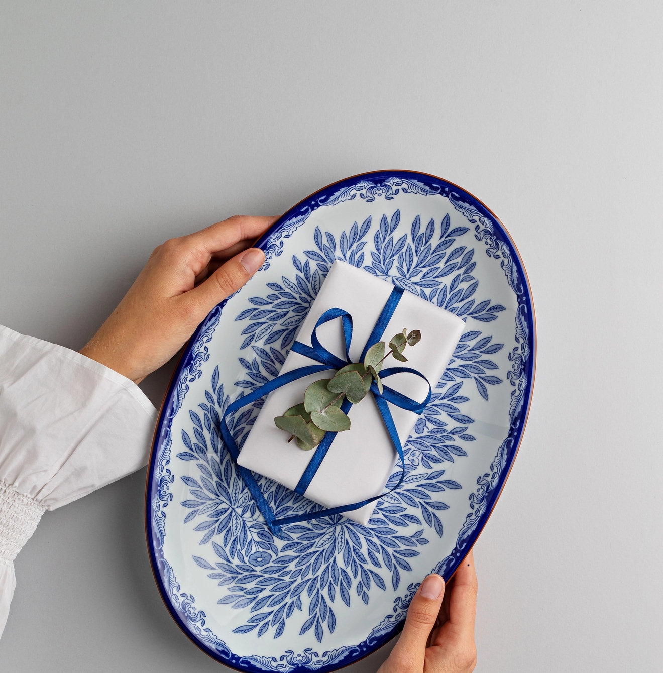 En kvinna som håller i ett uppläggningsfat i vitt och blått mönster med ett inslaget paket på.