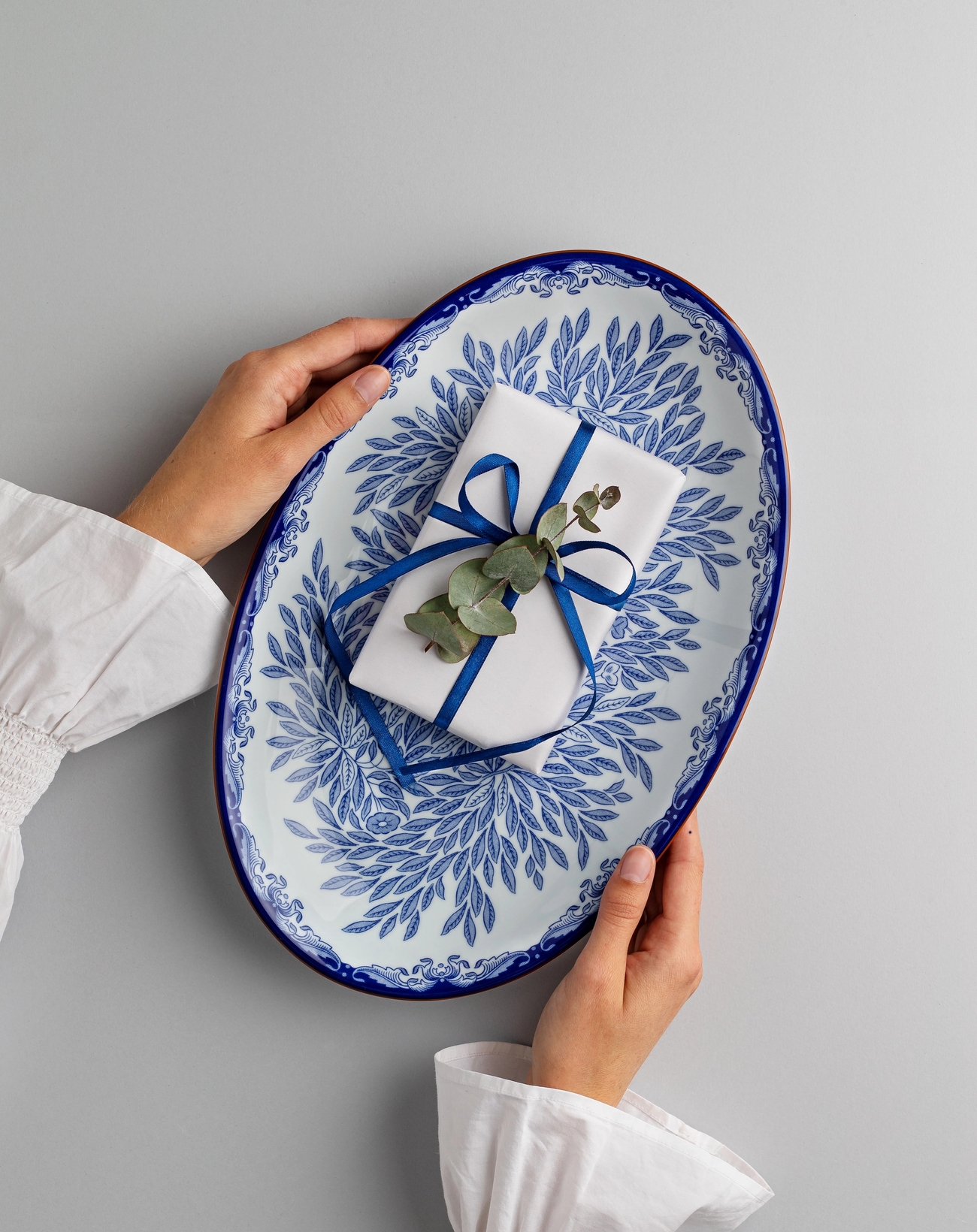 En kvinna som håller i ett uppläggningsfat i vitt och blått mönster med ett inslaget paket på.