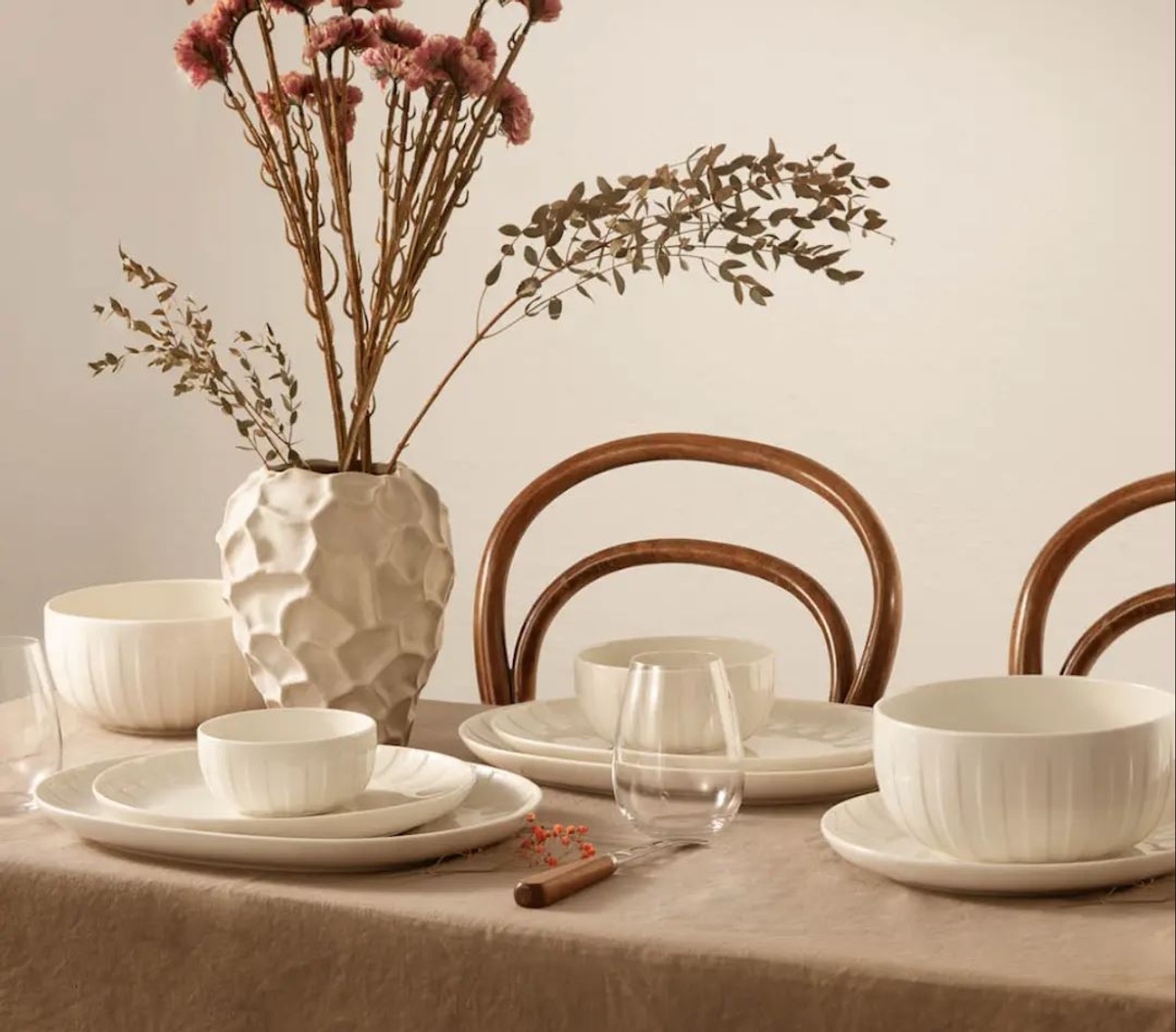a table with plates , bowls , glasses and a vase of flowers on it .