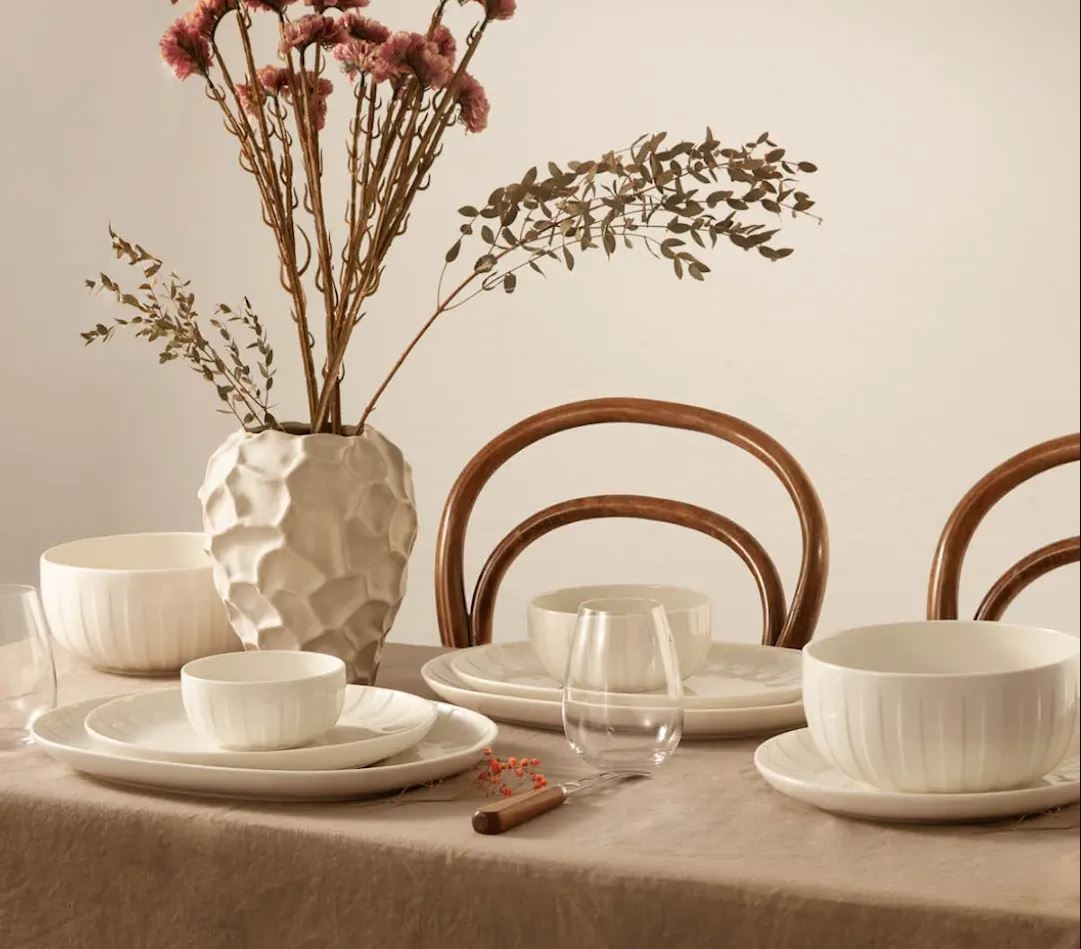 a table with plates , bowls , glasses and a vase of flowers on it .
