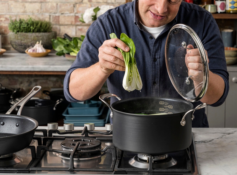 En stor svart kastrull på en spis som man lägger en pak choi i