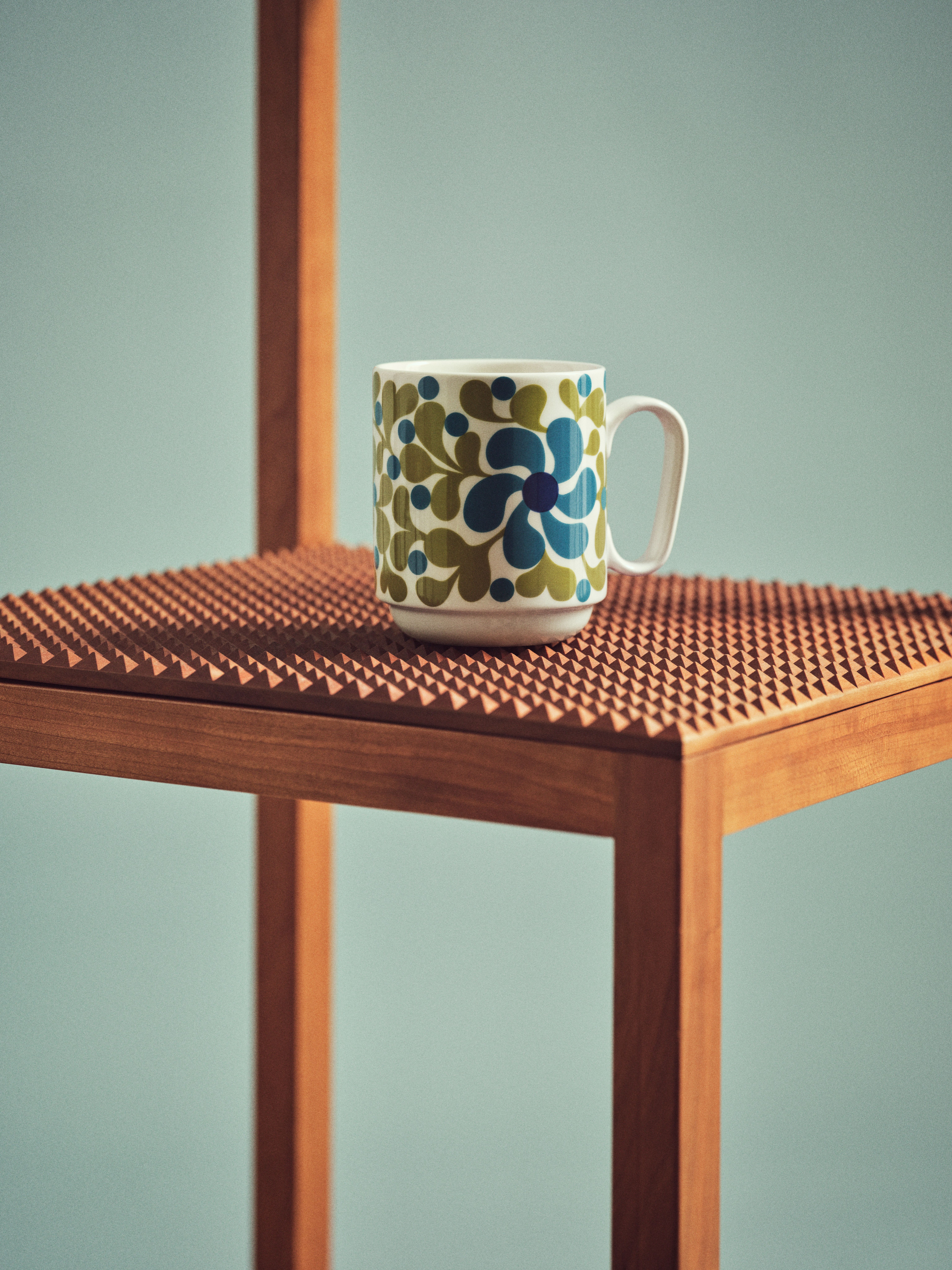 Mönstrad mugg i blått och grönt som står på en stol mot en turkos bakgrund