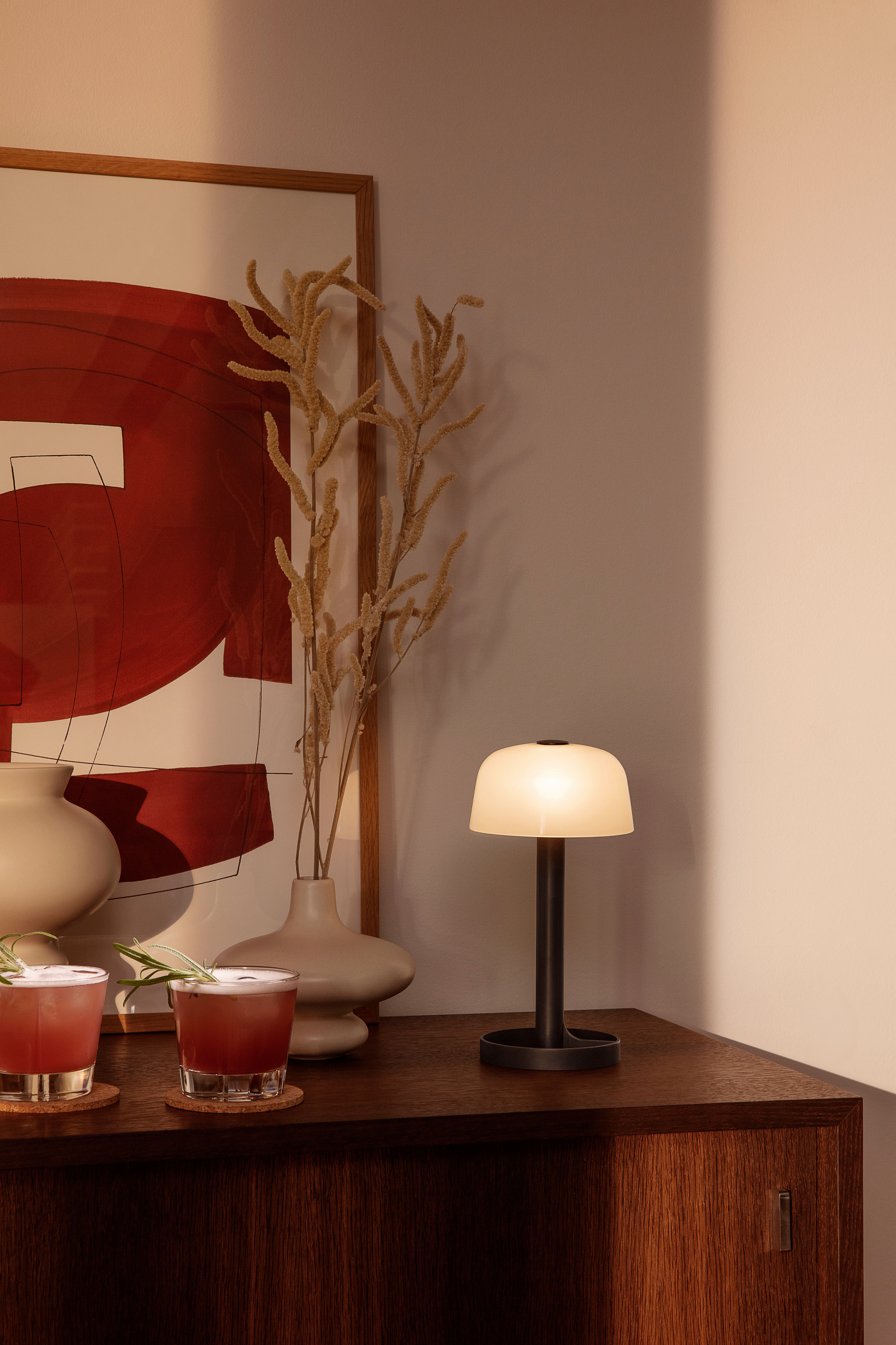 Mörkt träskivbord med två glas, en lampa och en beige vas på