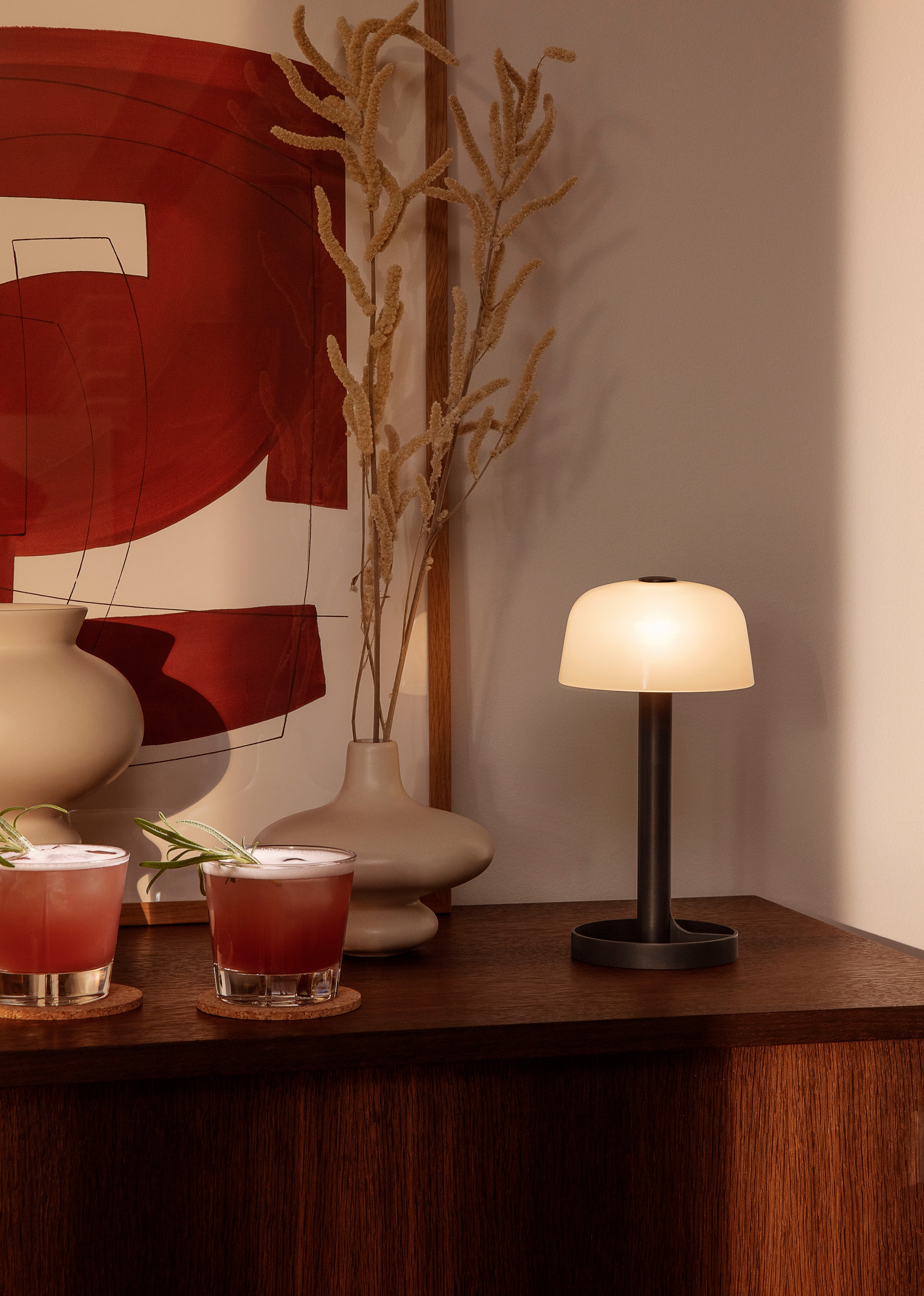 Mörkt träskivbord med två glas, en lampa och en beige vas på