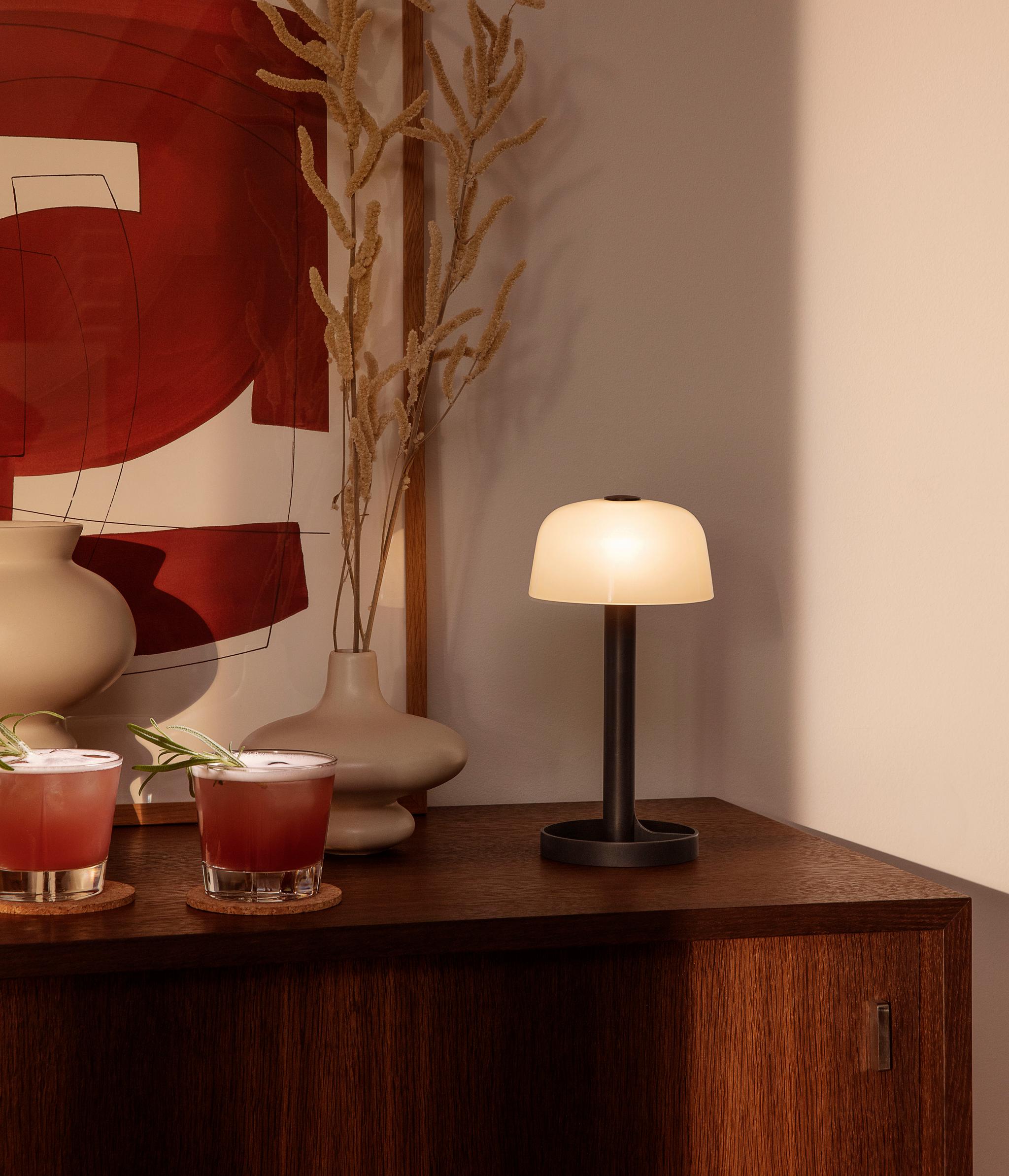 Två cocktails, dekorativa vaser, abstrakt konst och en lysande bordslampa på ett träskåp.