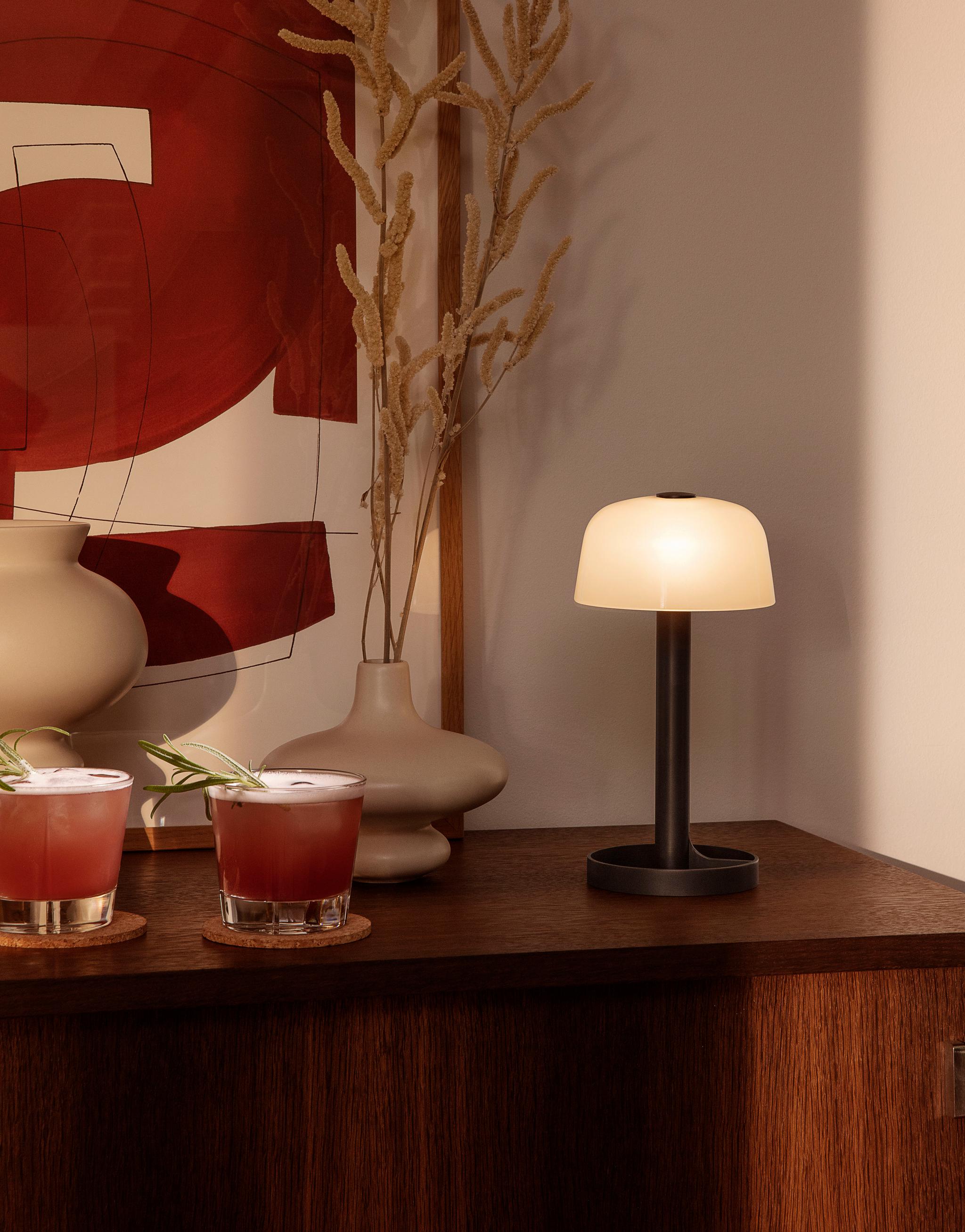 Mörkt träskivbord med två glas, en lampa och en beige vas på