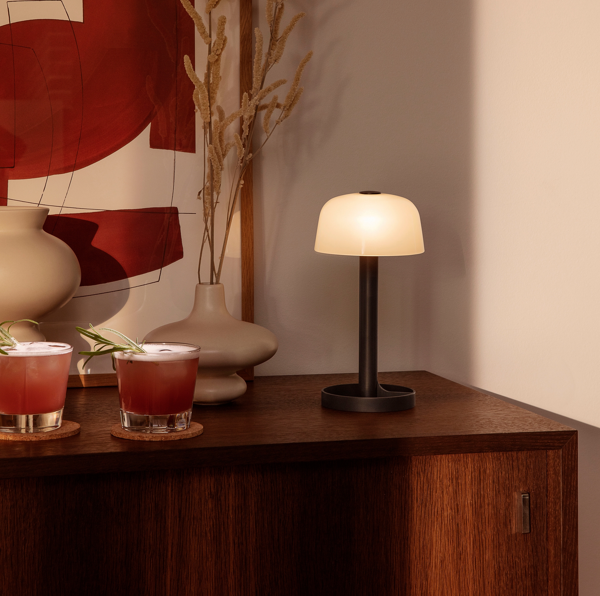 Mörkt träskivbord med två glas, en lampa och en beige vas på