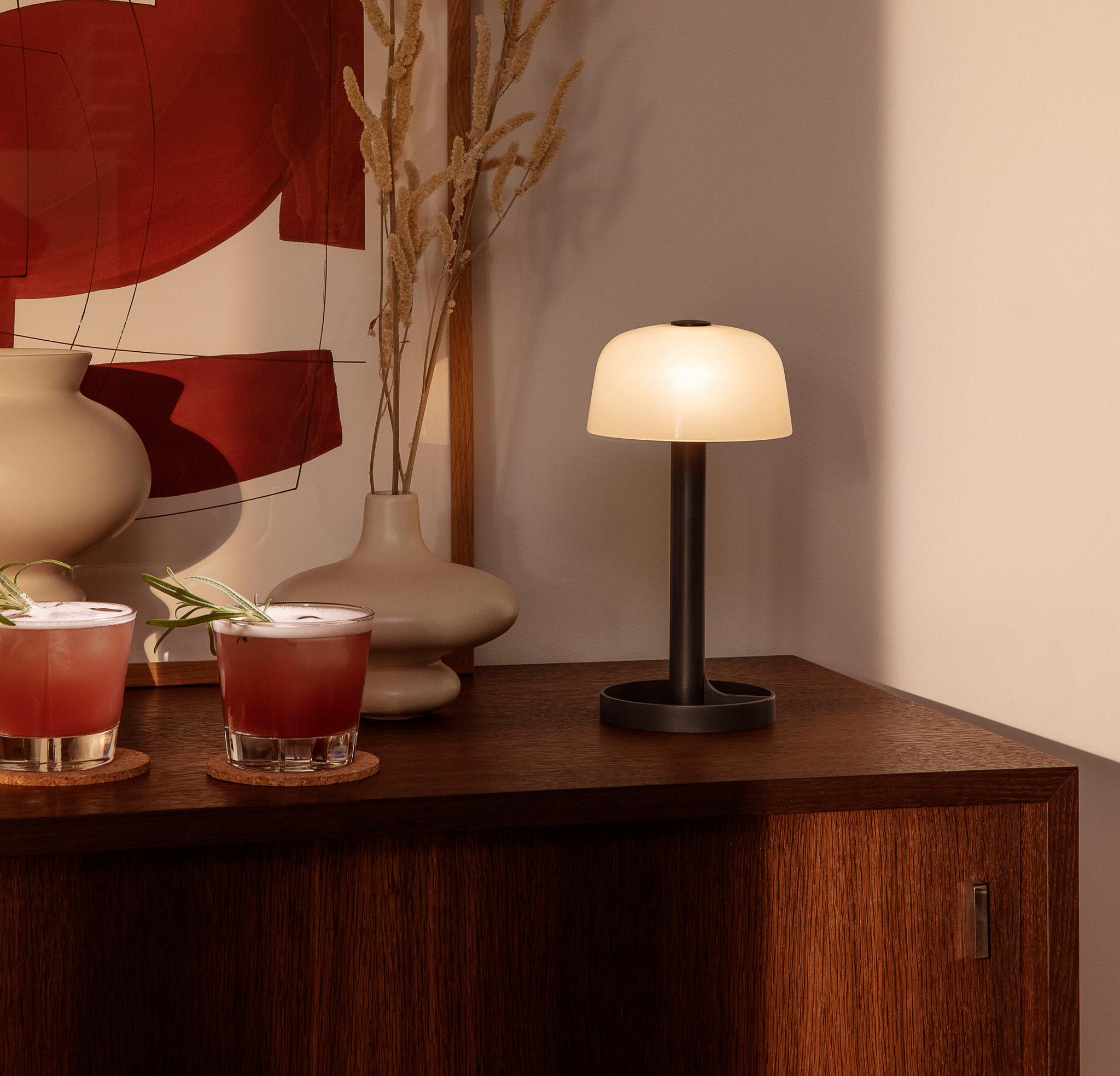 Mörkt träskivbord med två glas, en lampa och en beige vas på