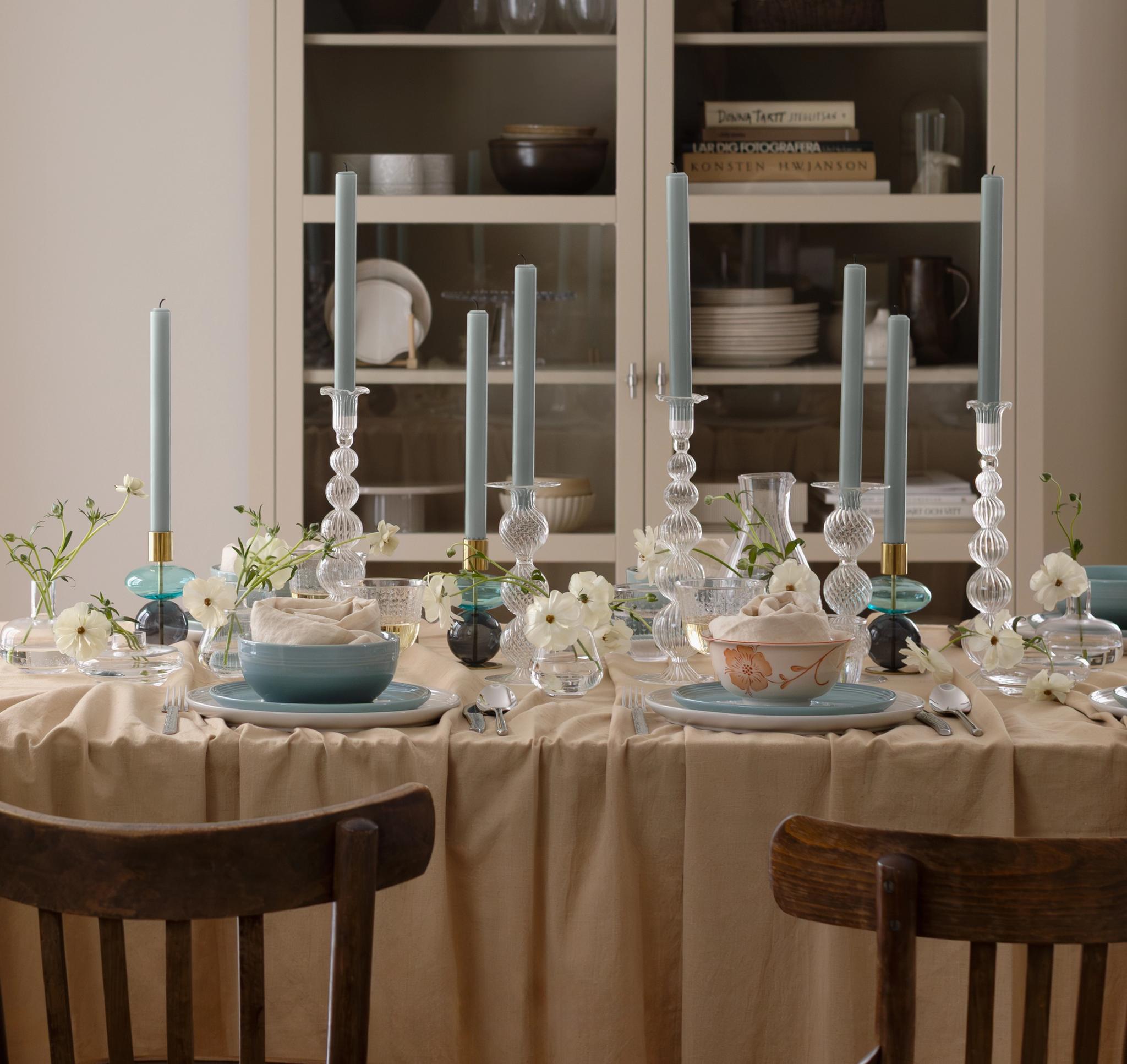 Et spisebord dekket med blå lys og hvite blomster, med en kjøkkenbenk på venstre side