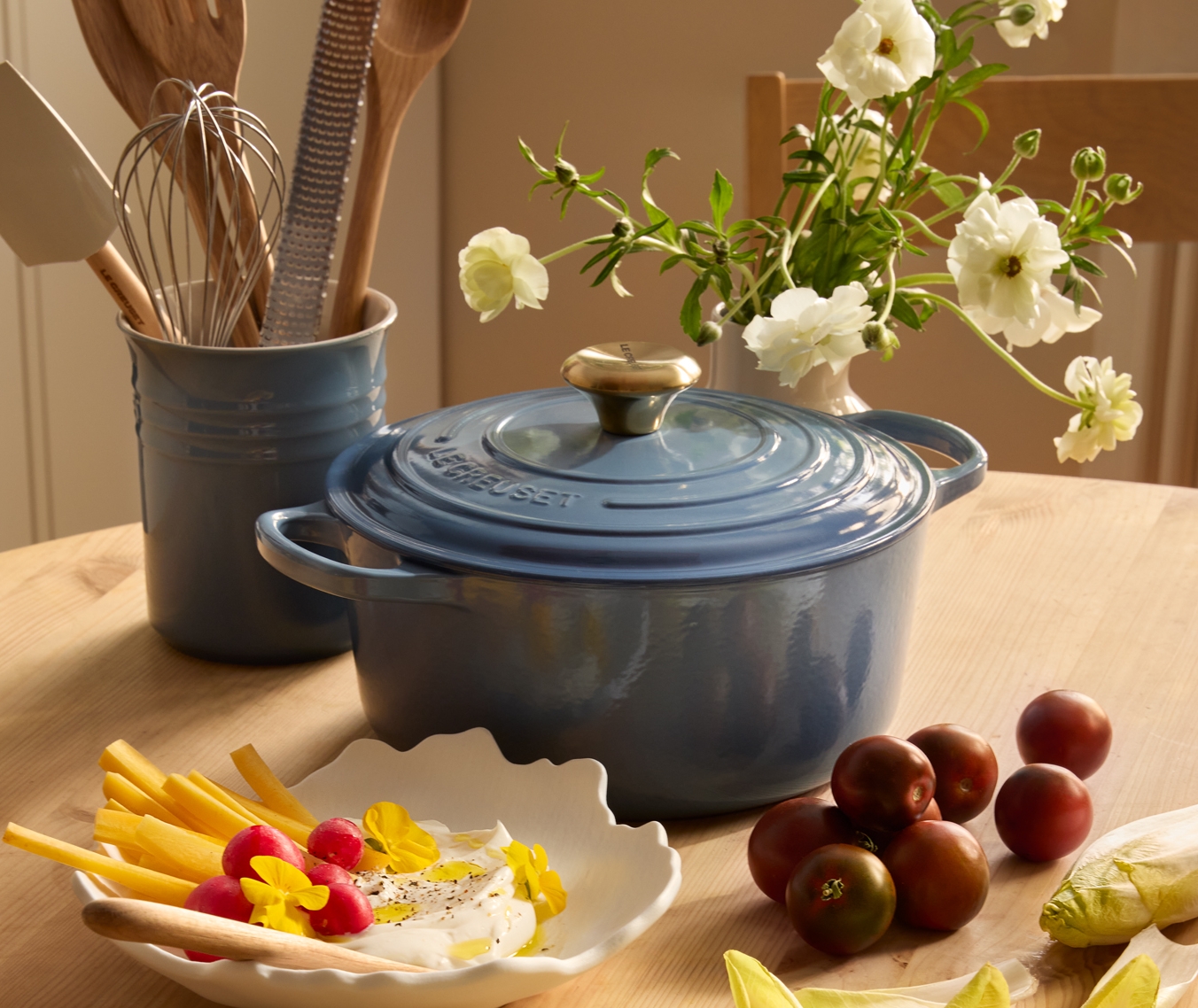 Keittiön pöydällä on sininen Le Creuset -kattila, kulhollinen dippikastiketta retiisien ja porkkanoiden kera, lautanen endiiviä ja leikkuulauta, jolla on magentanvärisiä pikkelöityjä munia.