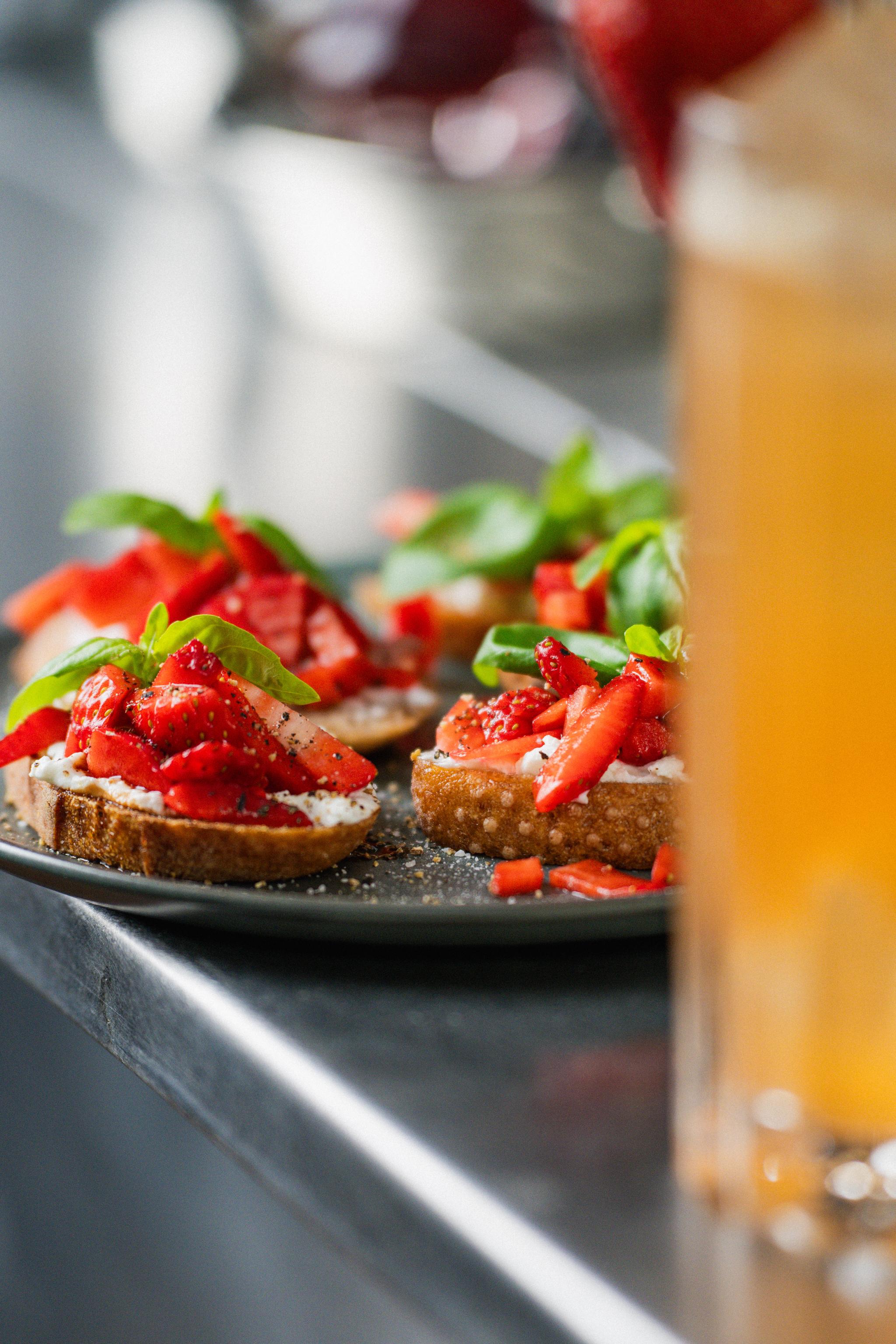 Närbild på crostini med färska jordgubbar, krämig ost och basilika på ett serveringsfat.