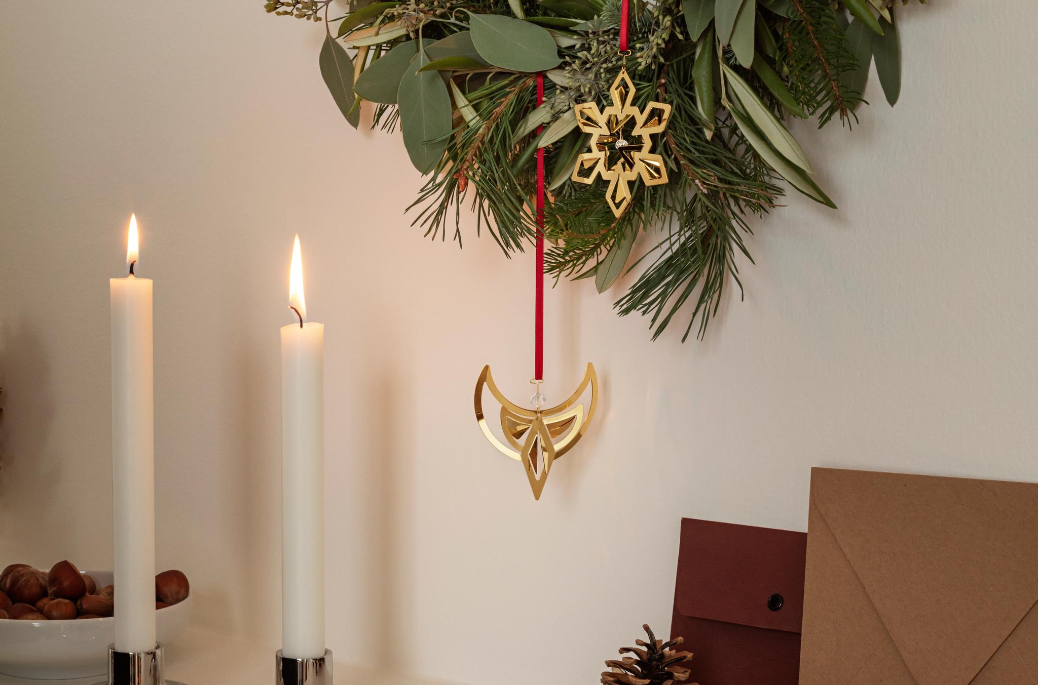 Grön julkrans med guldfärgade hängen ovanför tända ljus, kottar och röda julkulor.