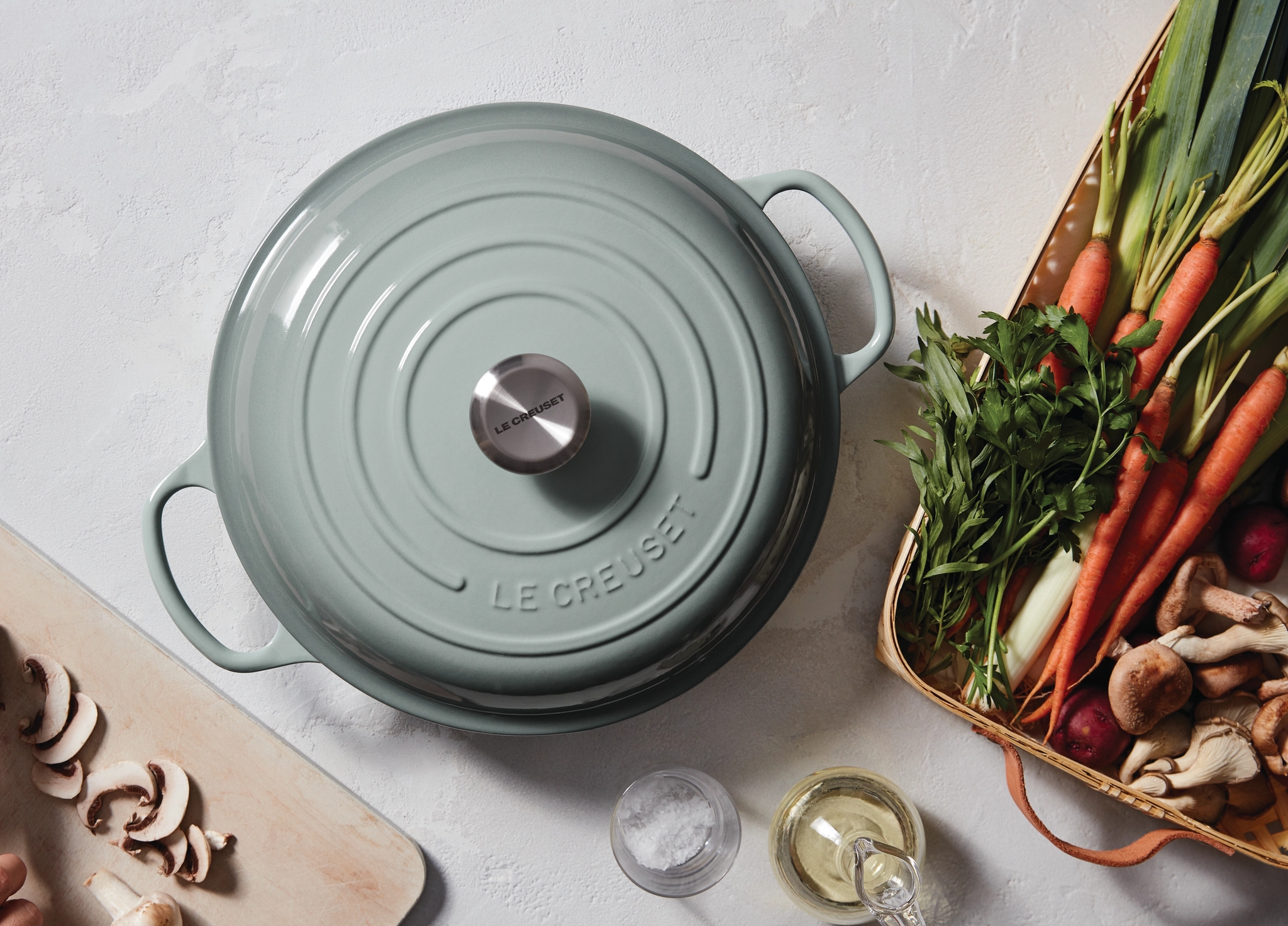 Vaaleanvihreä Le Creuset -pata keittiötasolla tuoreiden vihannesten ja sienien kanssa.