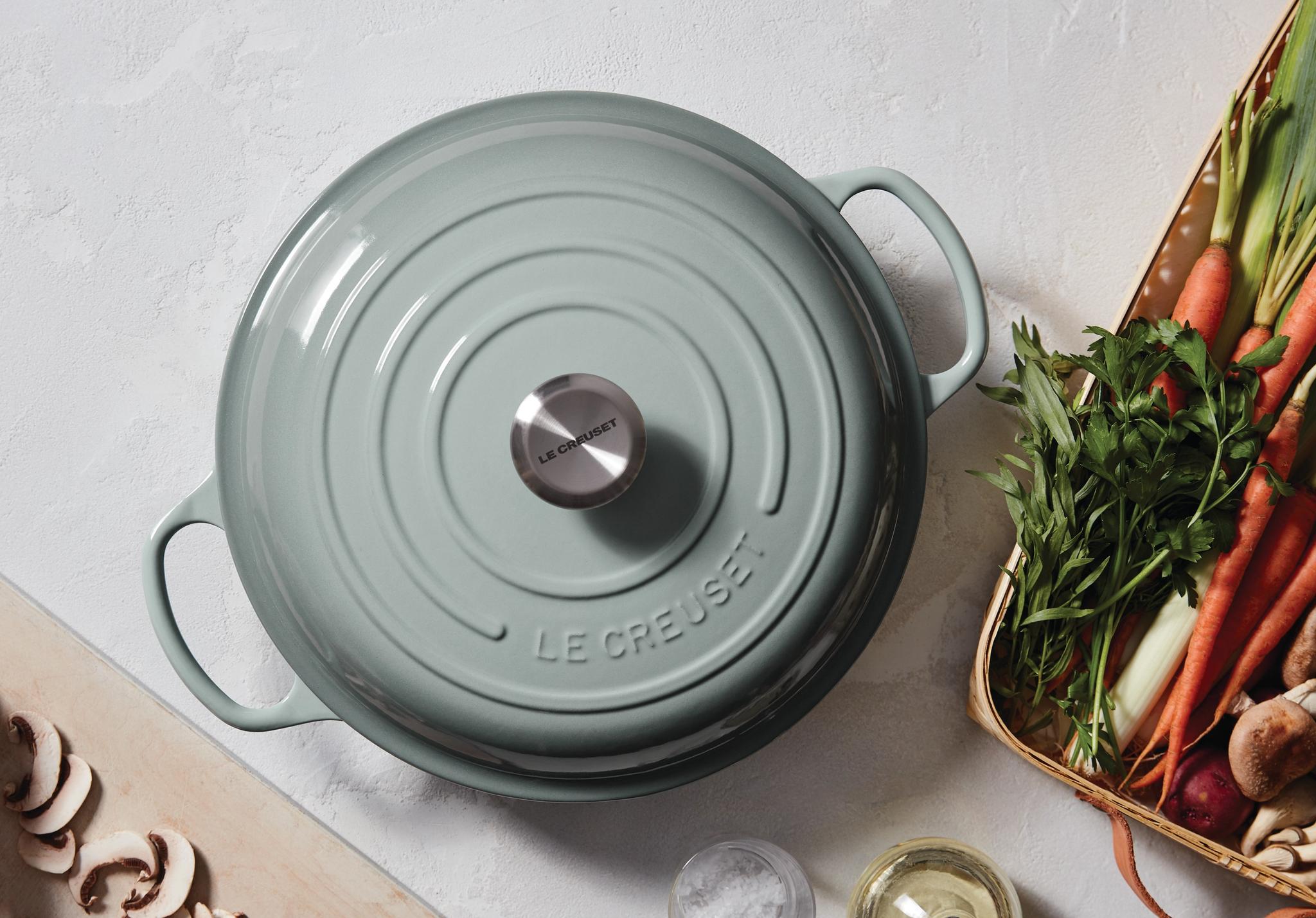 Vaaleanvihreä Le Creuset -pata keittiötasolla tuoreiden vihannesten ja sienien kanssa.