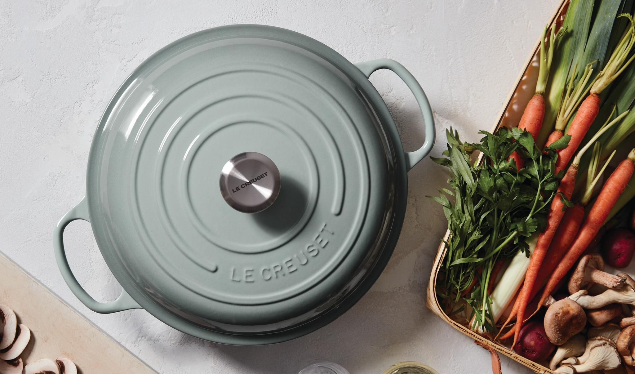 Vaaleanvihreä Le Creuset -pata keittiön tasolla tuoreiden vihannesten ja sienien kanssa ruoanlaittoa varten.