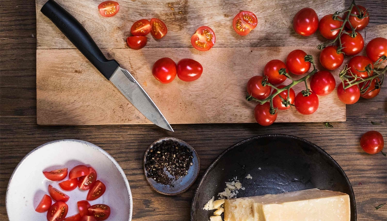Fiskars veitsi jolla on pilkottu tomaatteja puisella leikkuulaudalla