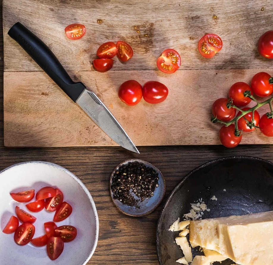 Fiskars veitsi jolla on pilkottu tomaatteja puisella leikkuulaudalla