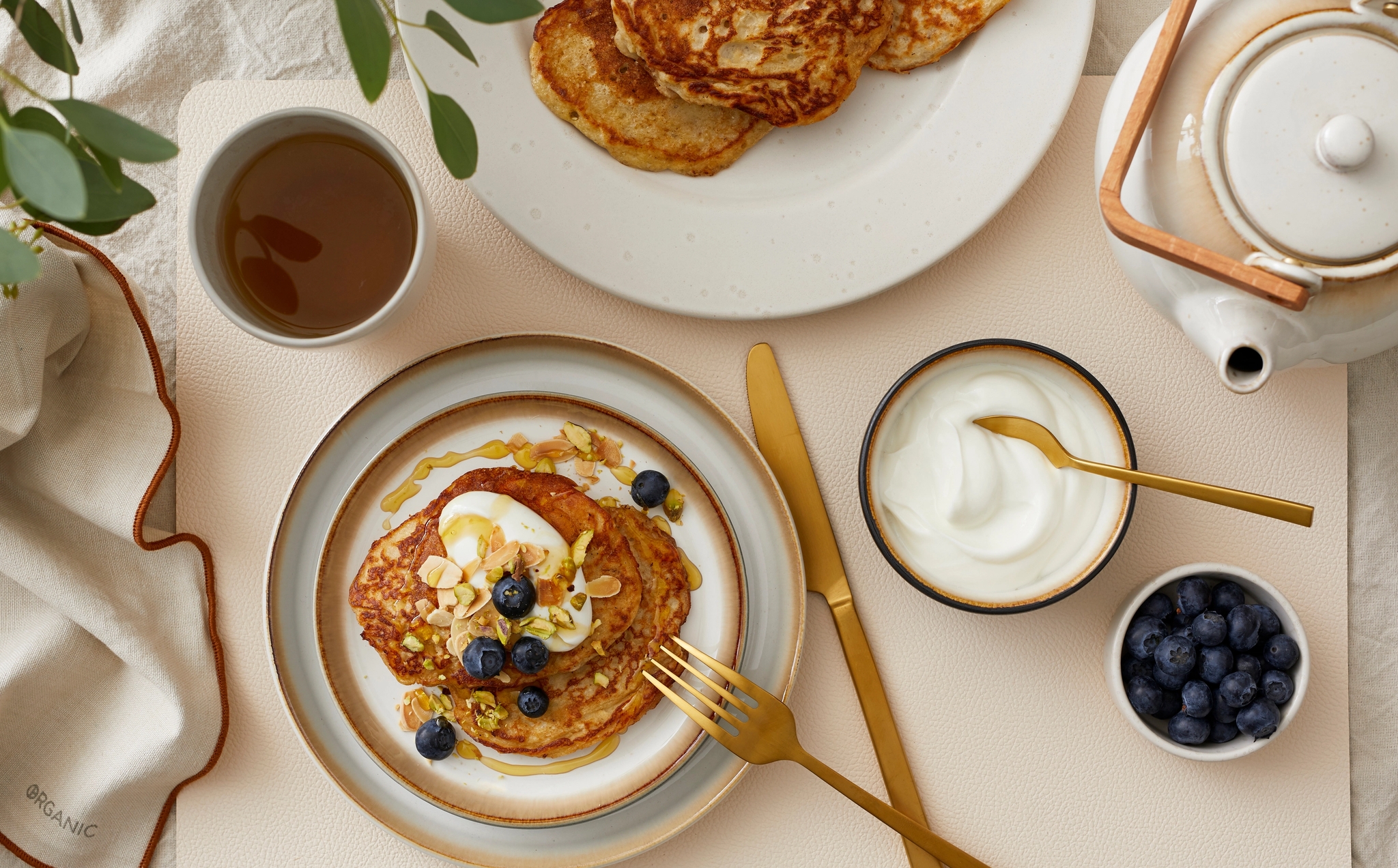 Lyxig frukost med pannkakor toppade med blåbär, nötter och yoghurt, serverade med te på ett dukat bord.