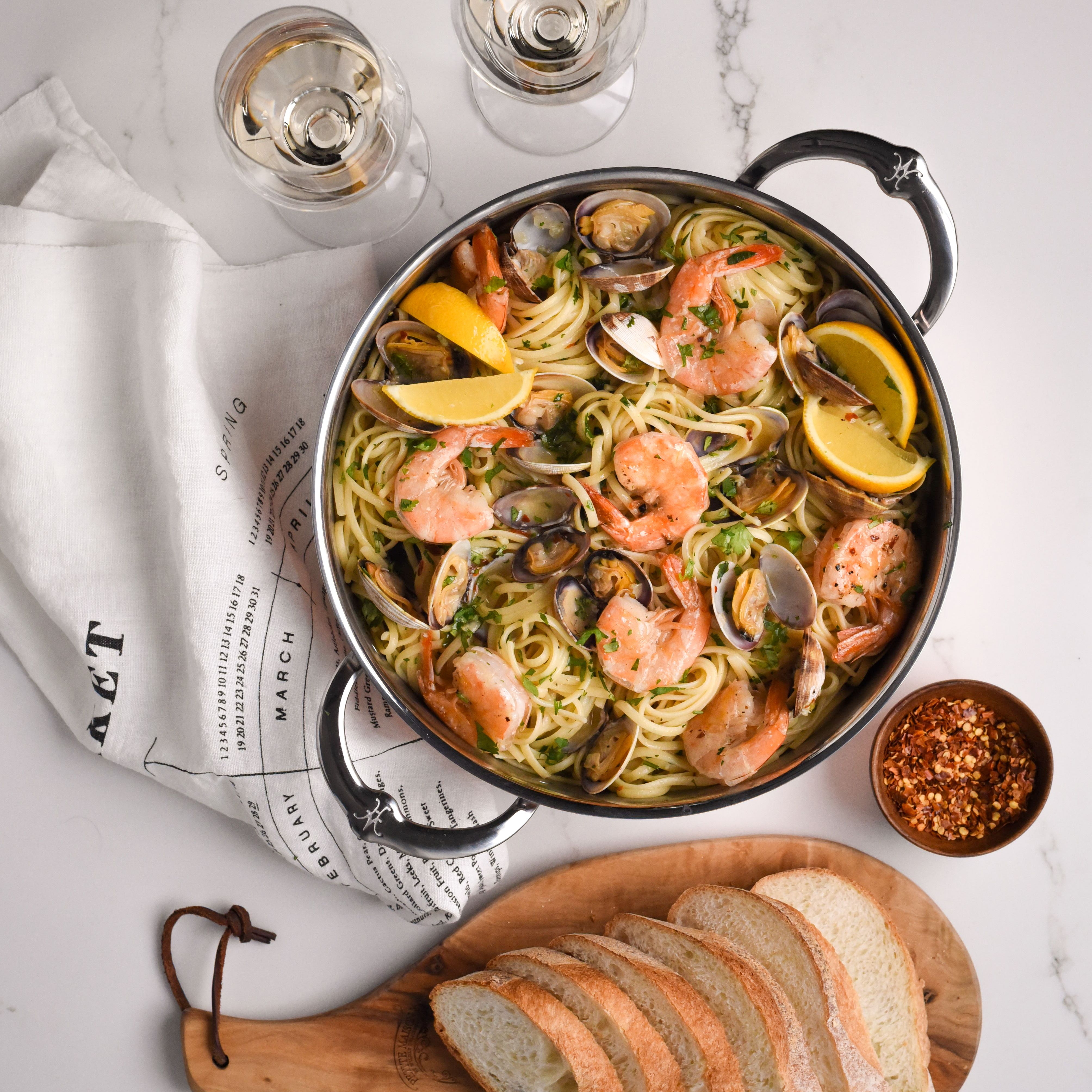 Pastaa katkarapujen ja simpukoiden kanssa kattilassa, tarjoillaan leivän, viinin ja chilijauheen kera.