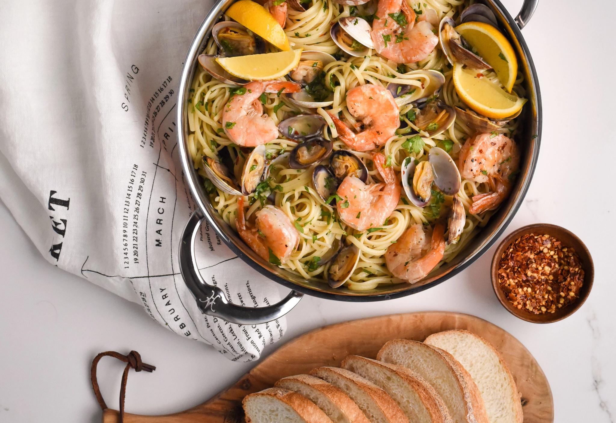 Pastaa katkarapujen ja simpukoiden kanssa kattilassa, tarjoillaan leivän, viinin ja chilijauheen kera.