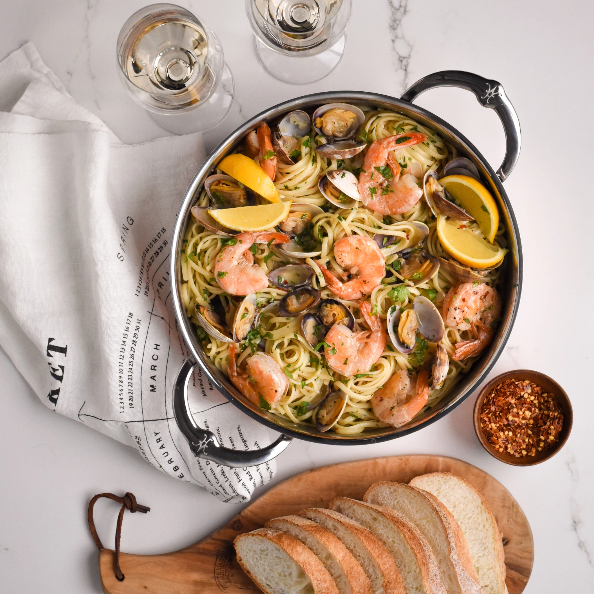 Pastaa katkarapujen ja simpukoiden kanssa kattilassa, tarjoillaan leivän, viinin ja chilijauheen kera.