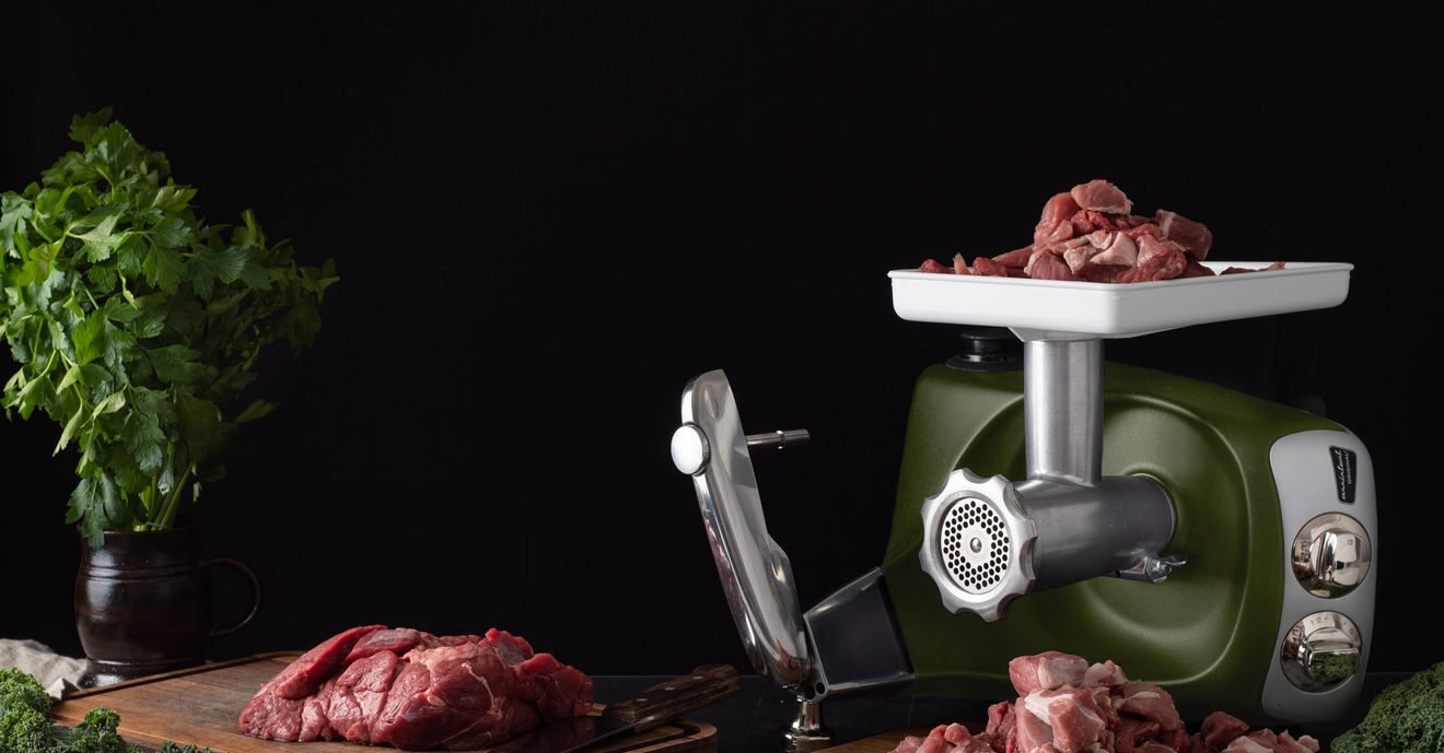 Lihamylly ja raa'at lihapalat puisella leikkuulaudalla