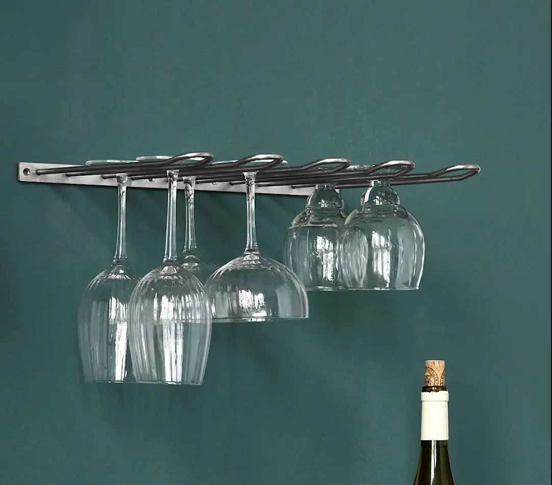 Five wine glasses hanging from a metal rack on a dark teal wall, with a wine bottle partially visible below.