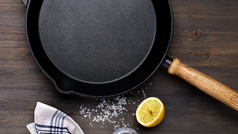 a cast iron skillet with a wooden handle and a slice of lemon on a wooden table .
