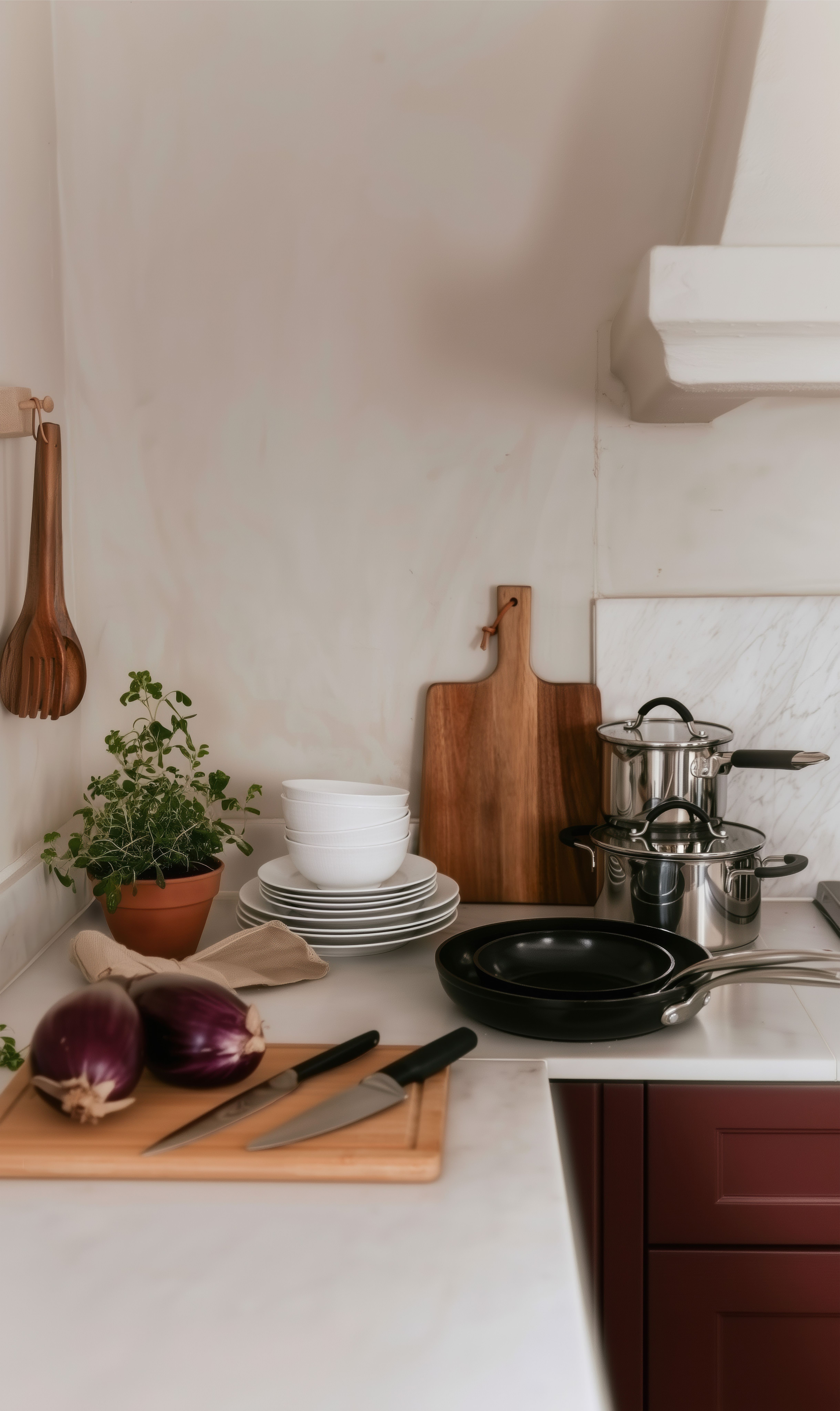 Köksbänk med aubergine, knivar, staplade tallrikar, grytor, stekpannor och en krukväxt.