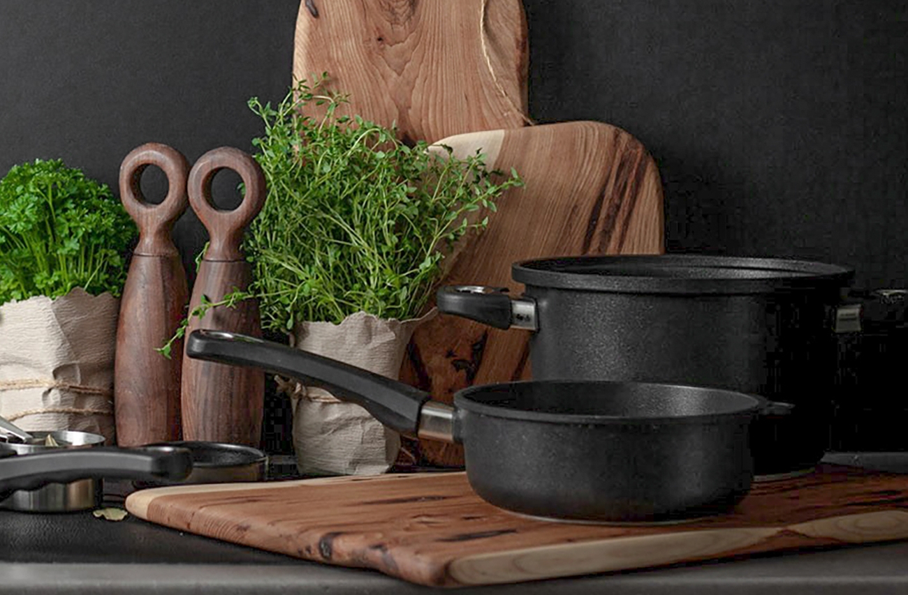 AMT Gastroguss olika svarta kastruller och stekpannor utställda i ett kök med bruna trä brickor