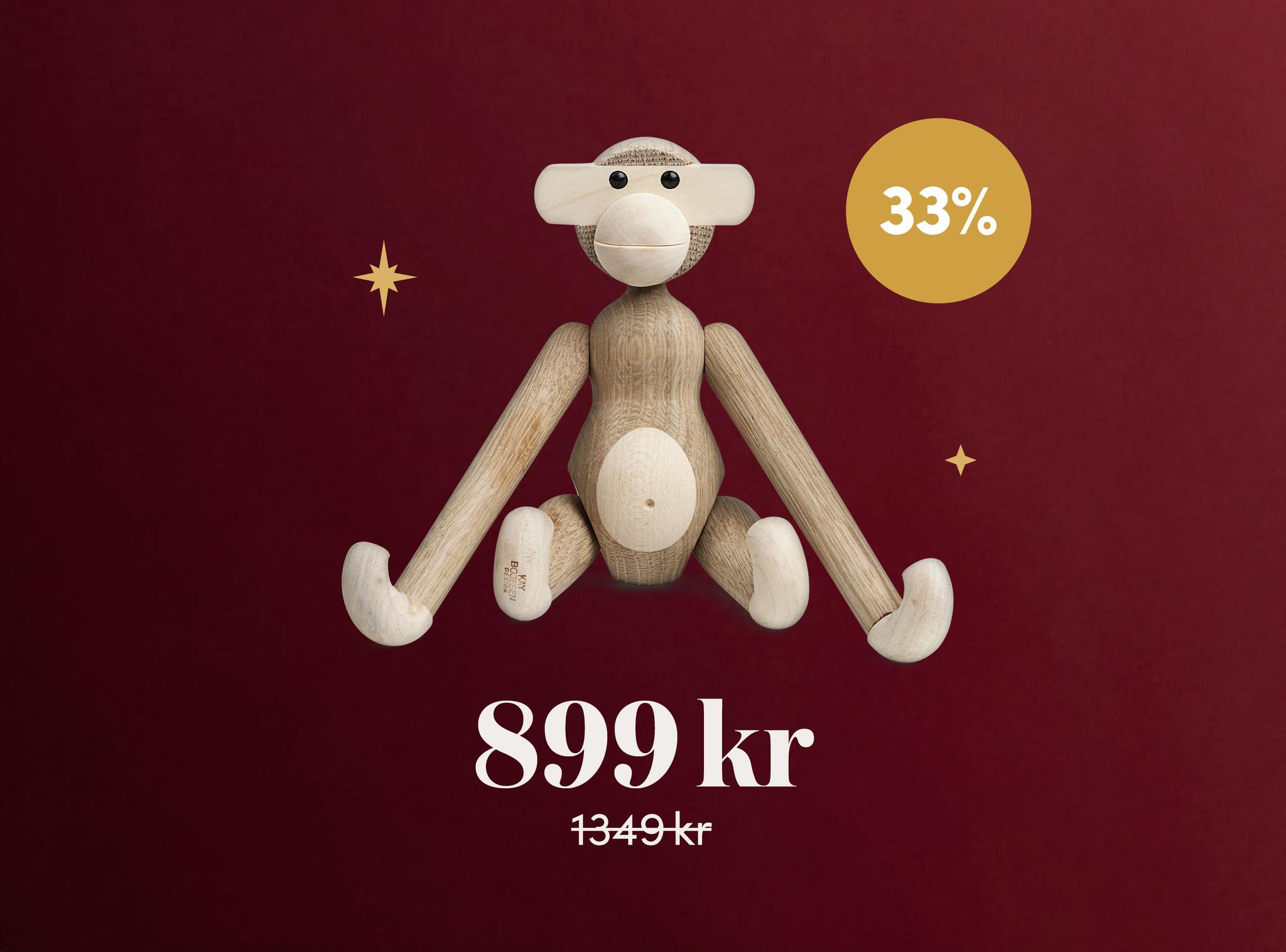 A wooden monkey toy on a dark red background with a gold "33%" off circle, priced at 899 kr, down from 1349 kr.