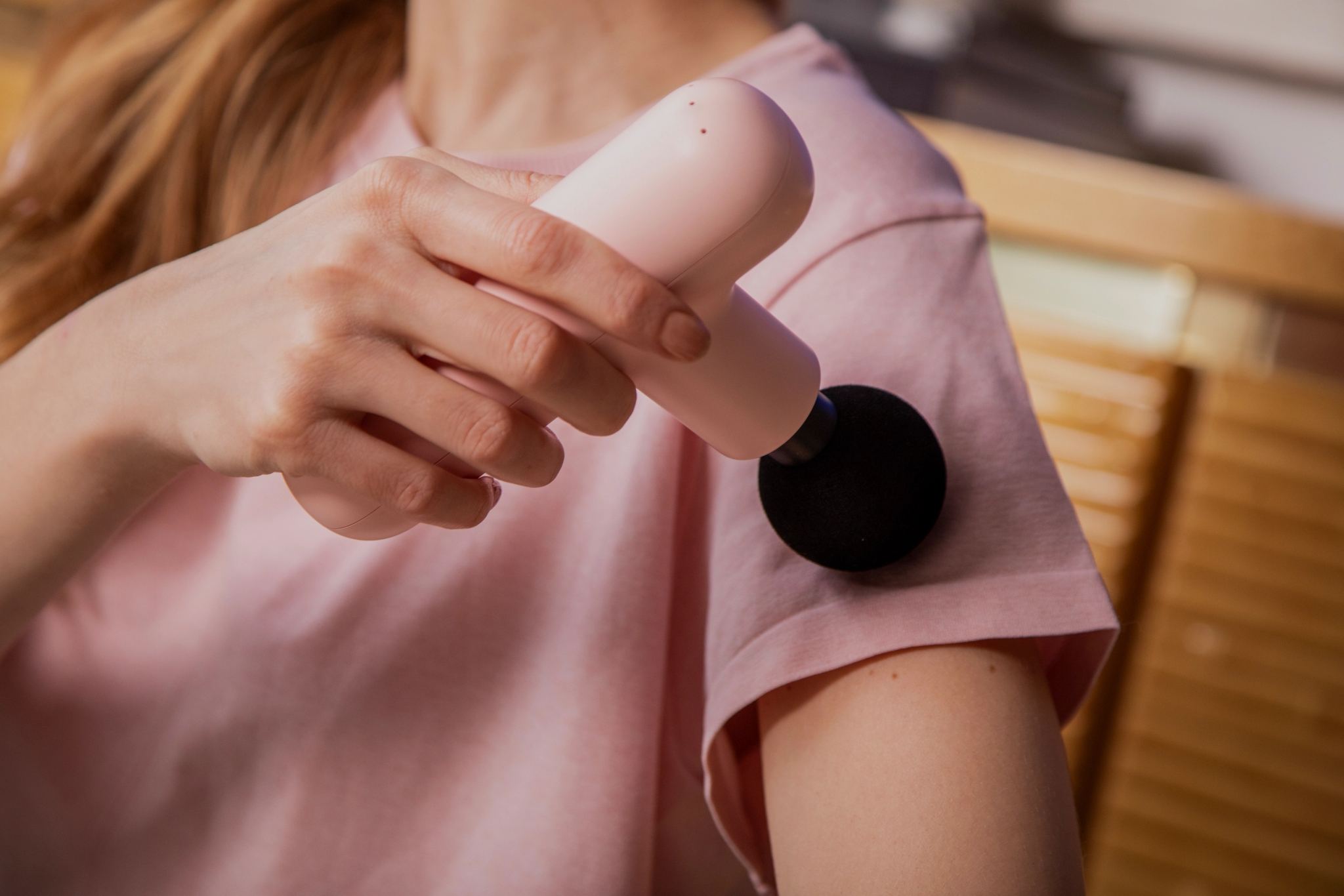 En kvinna använder en massagepistol för att massera musklerna i axeln