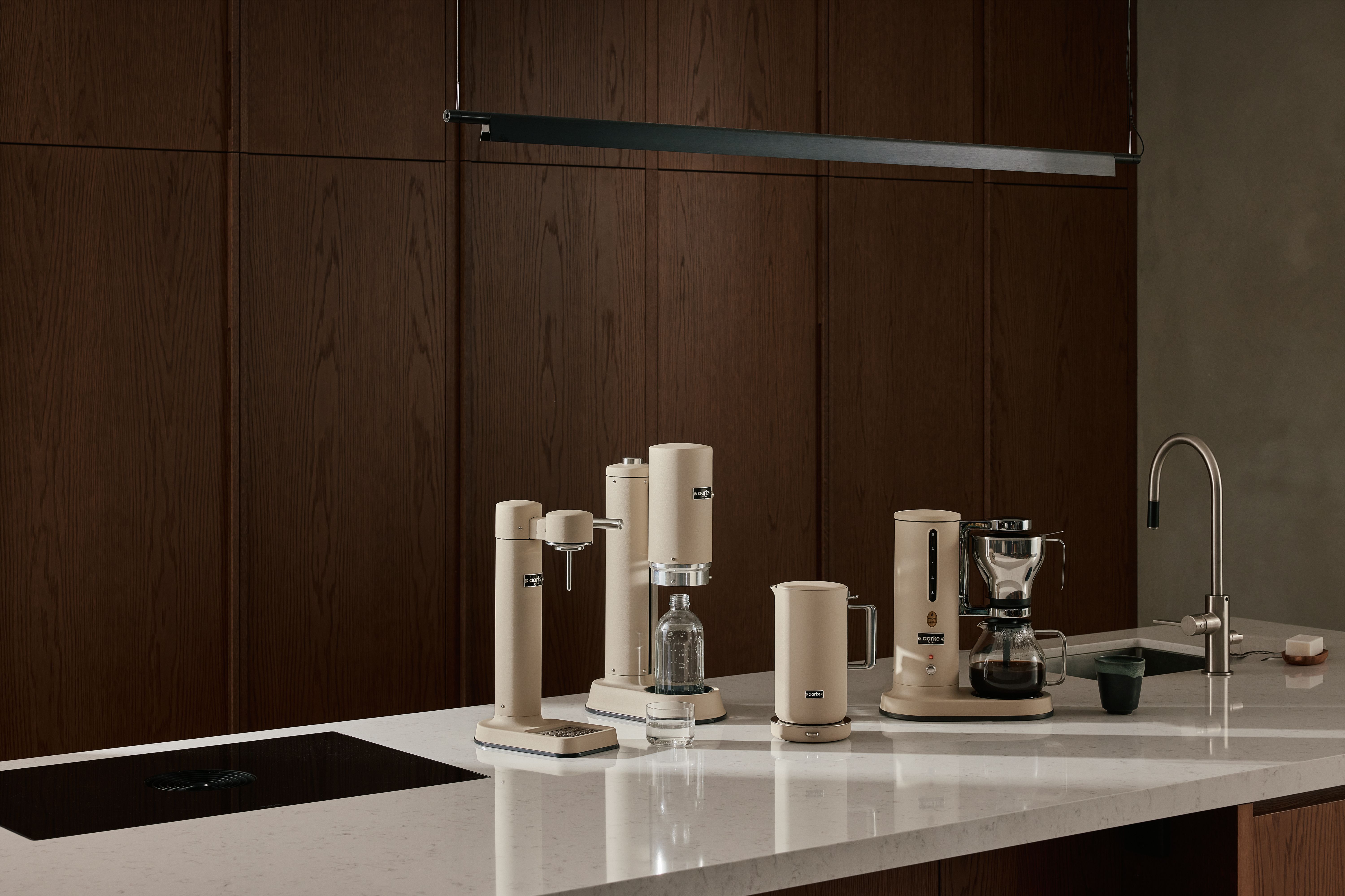 Stilren modern köksbänk med beige köksmaskiner för kaffe, vatten och dryck mot mörka träskåp.