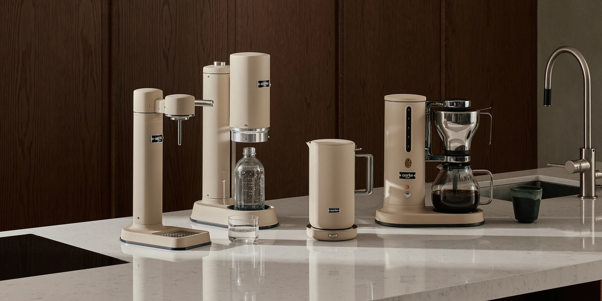 Stilren modern köksbänk med beige köksmaskiner för kaffe, vatten och dryck mot mörka träskåp.