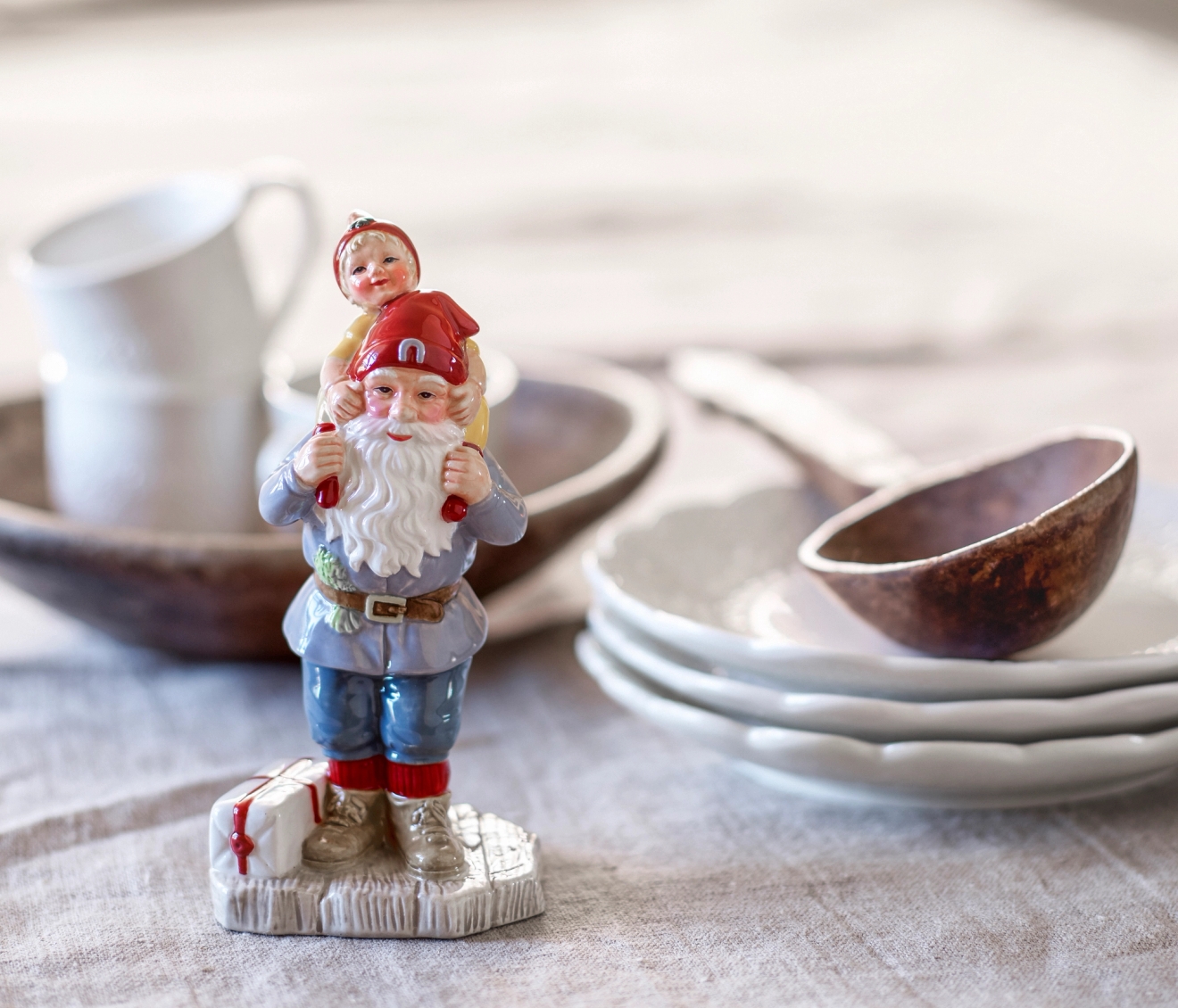 Cult design tomte som har ett barn på axlarna utpalcerad på ett bord med grå duk och gråa tallrikar