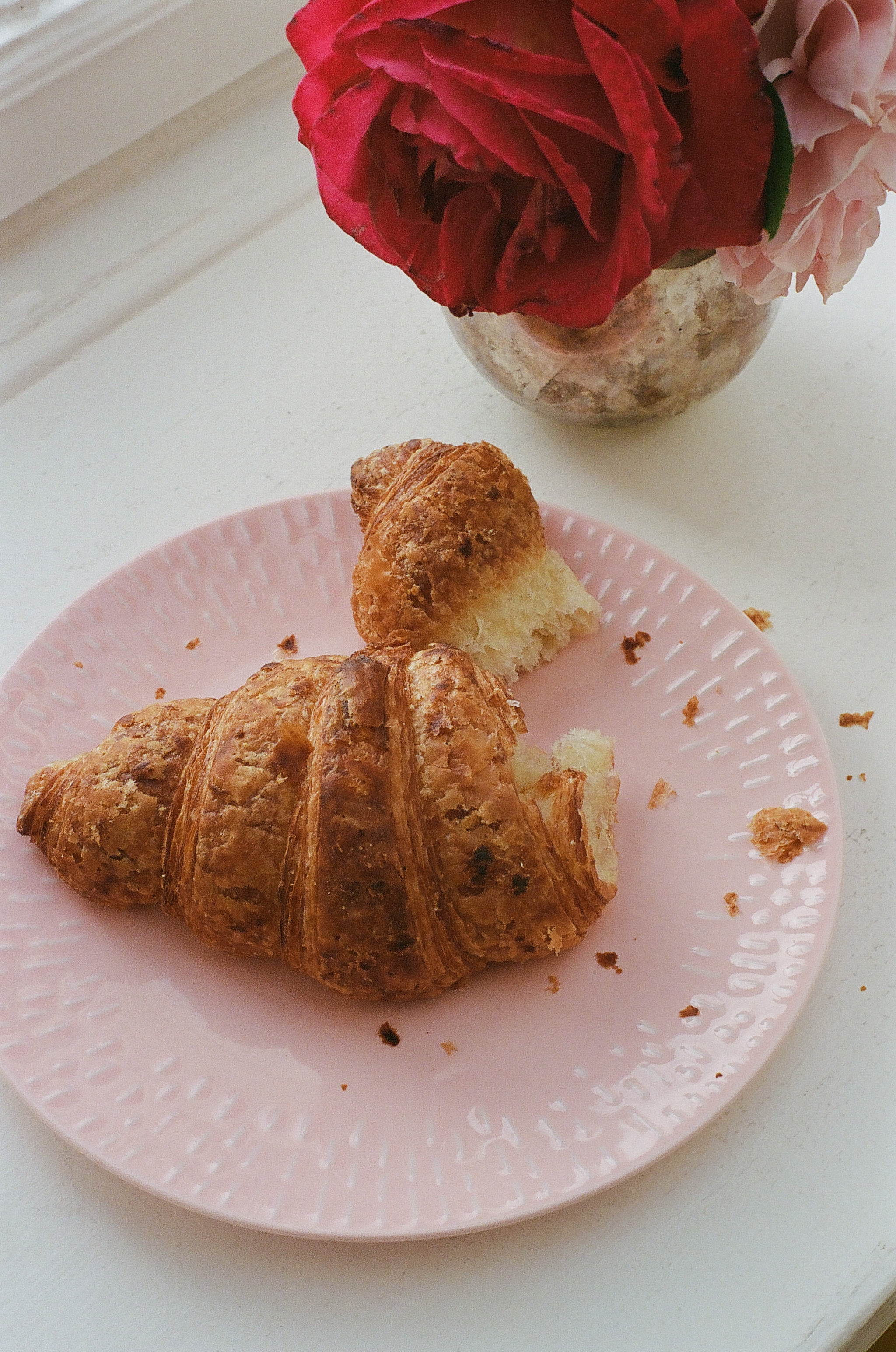 Nystekt croissant på rosa tallerken ved siden av en vase med røde roser.