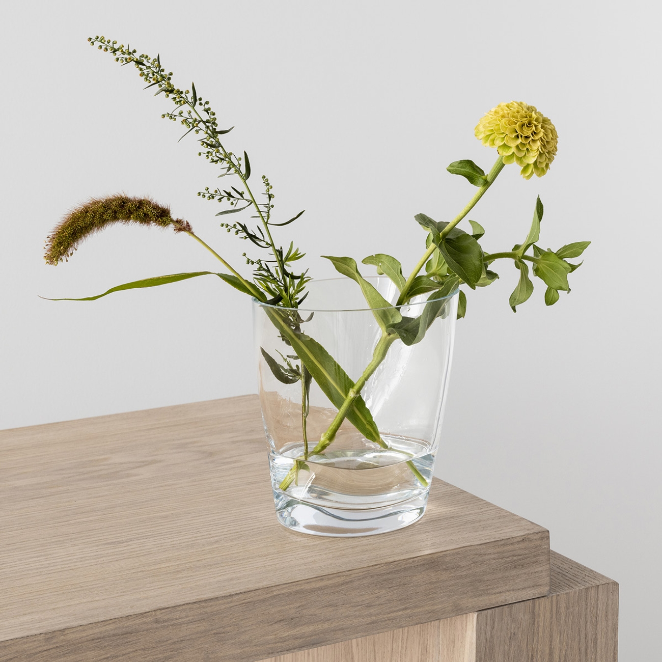 Orrefors vas på ett ljust träbord med en enklare bukett i sig