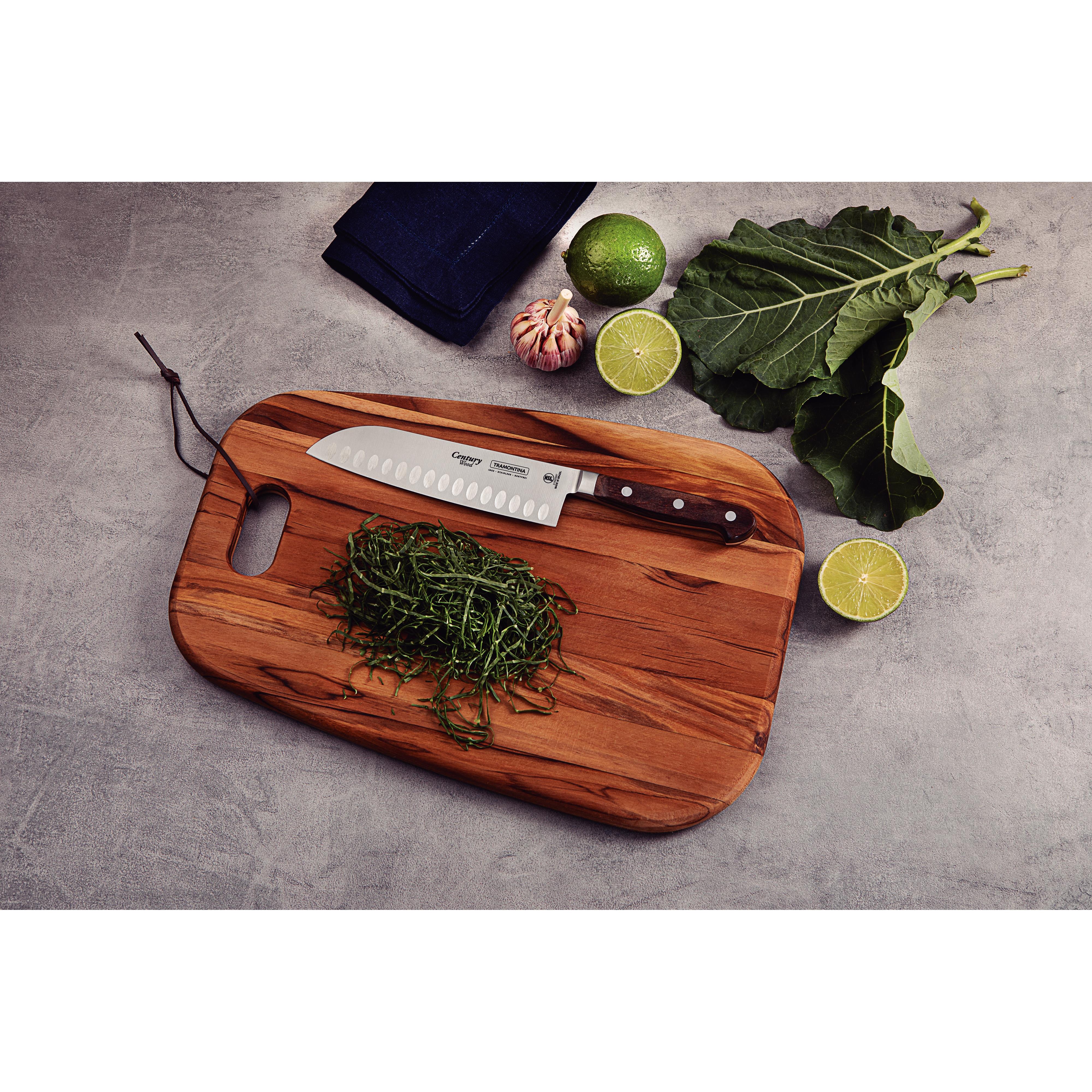 Kockkniv och strimlade gröna blad på en träskärbräda, omgivna av lime, vitlök och grönkål.