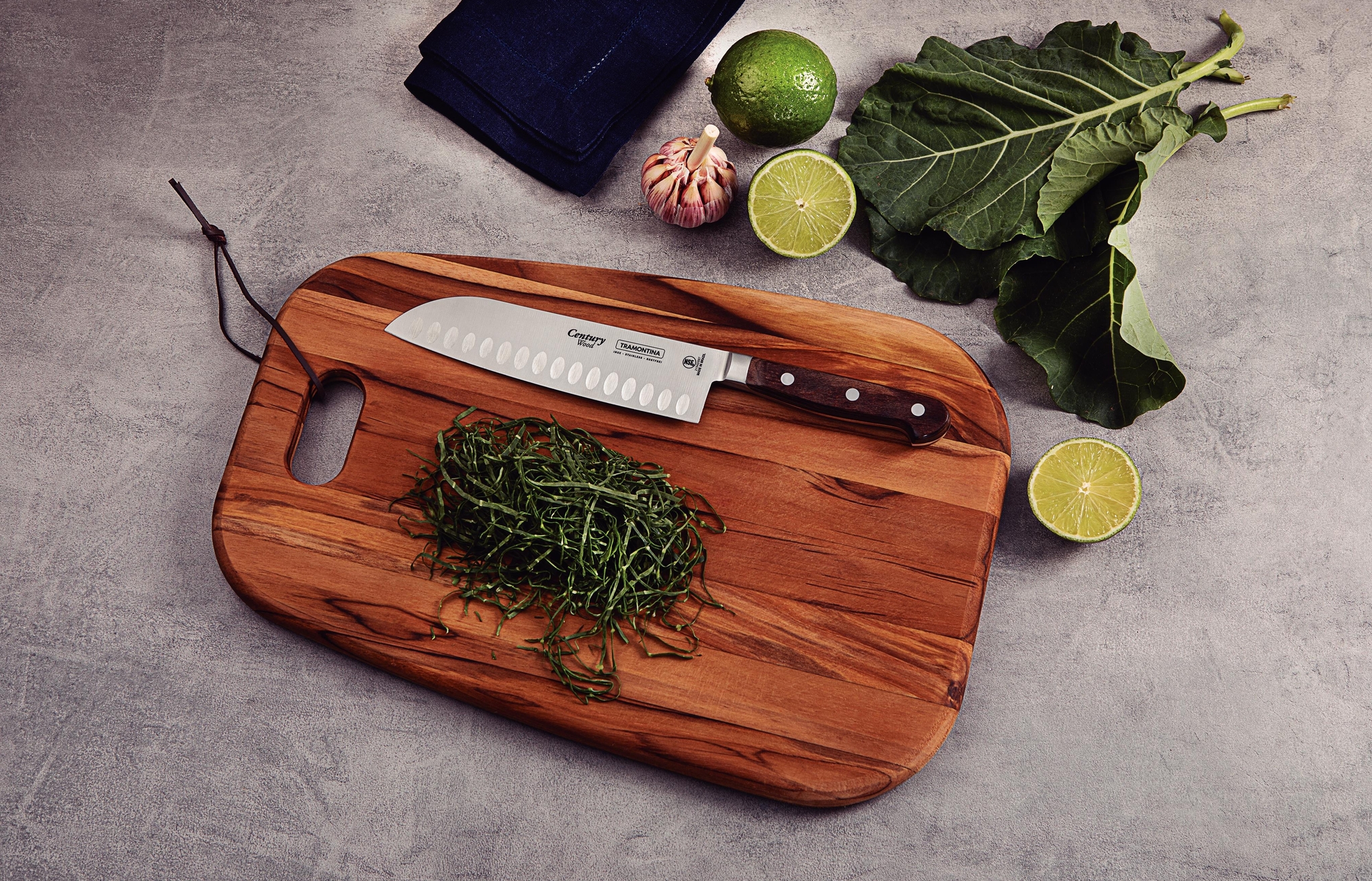 Kockkniv och strimlade gröna blad på en träskärbräda, omgivna av lime, vitlök och grönkål.