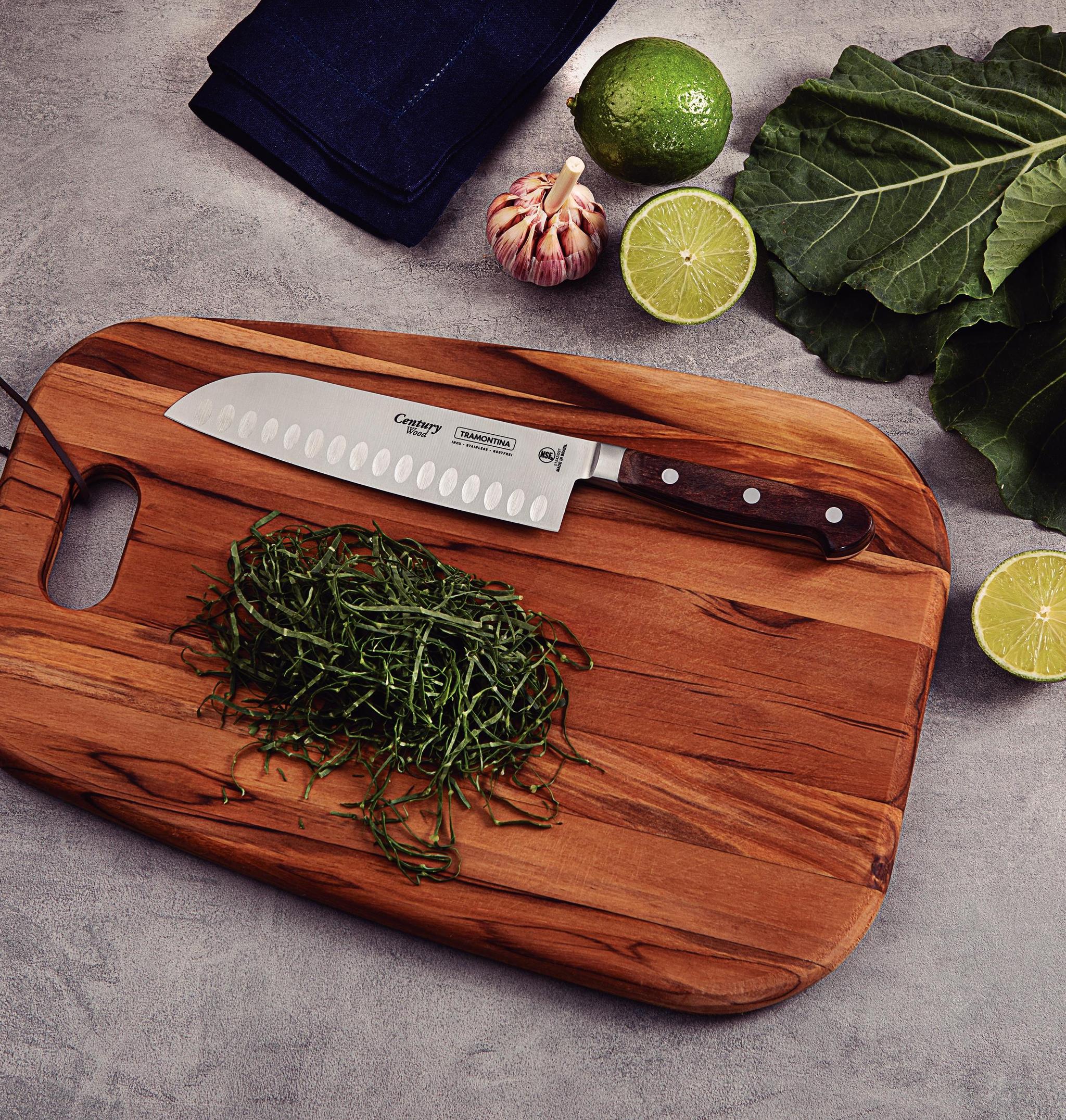 Kockkniv och strimlade gröna blad på en träskärbräda, omgivna av lime, vitlök och grönkål.