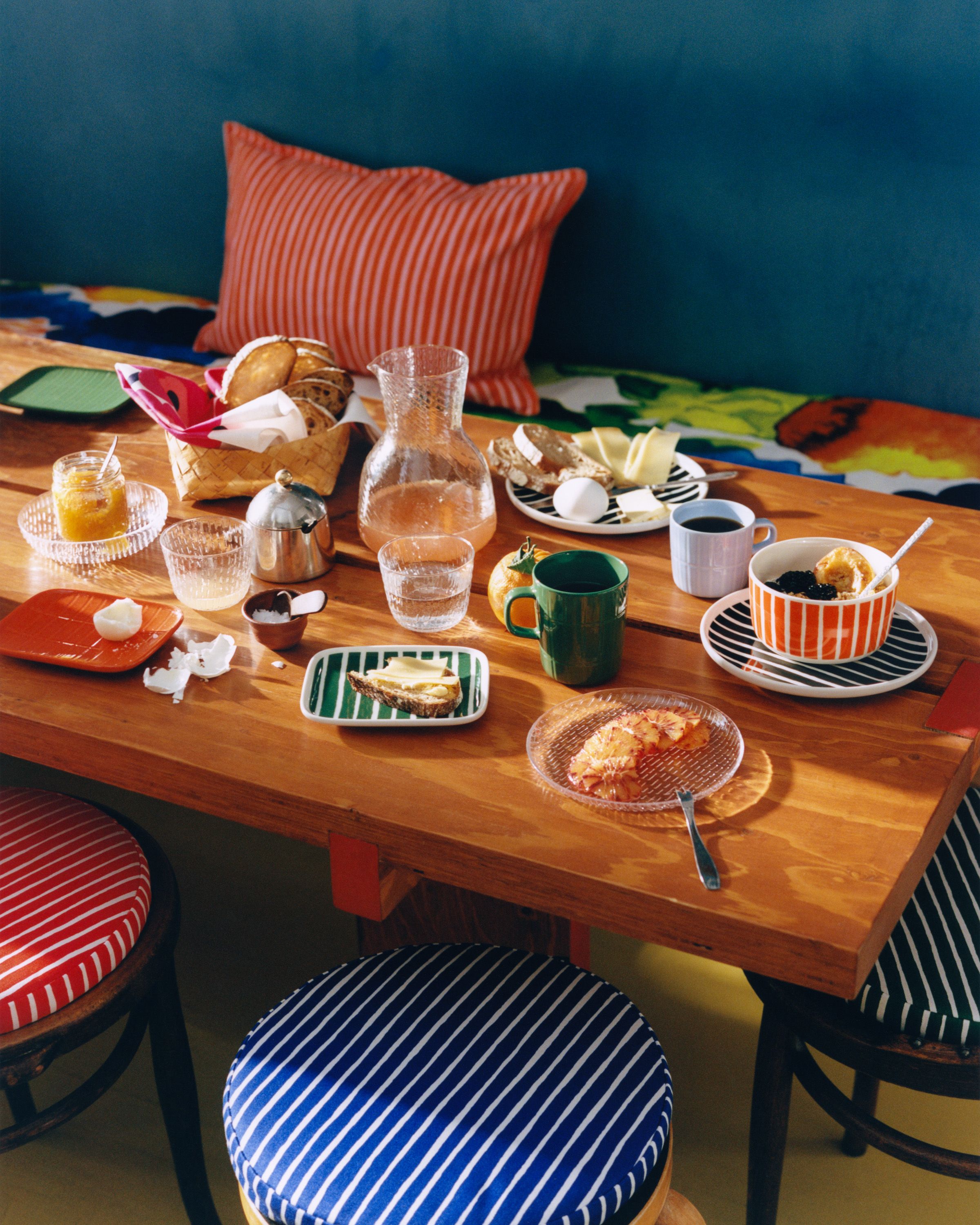 Färgglad frukostdukning på ett träbord med randiga textilier, porslin och olika frukosträtter.