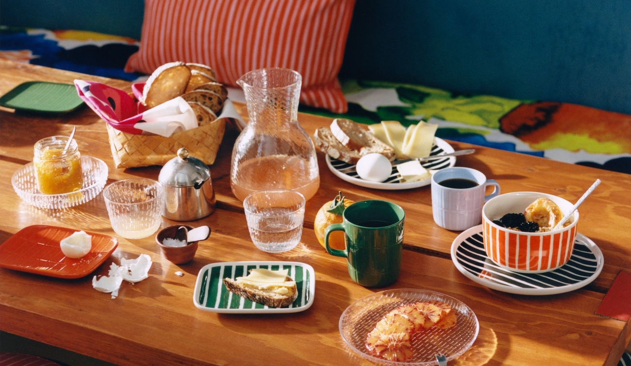 Färgglad frukostdukning på ett träbord med randiga textilier, porslin och olika frukosträtter.