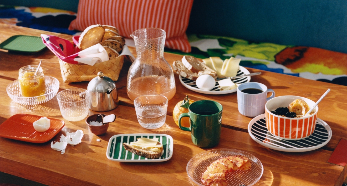 Färgglad frukostdukning på ett träbord med kaffe, bröd, ägg och randiga textilier.