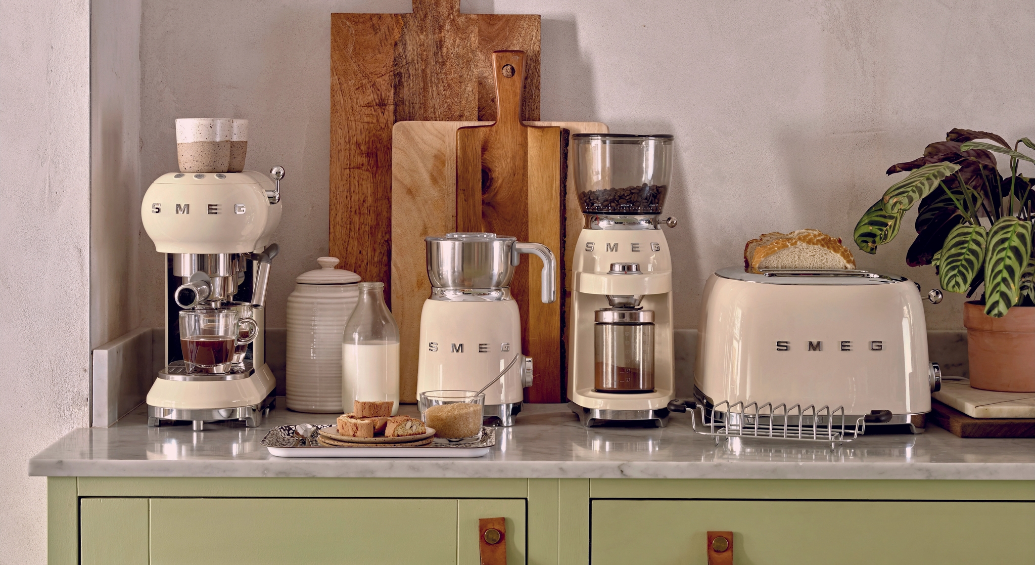 Stilren kjøkkenbenk med kremfargede SMEG-kjøkkenapparater, skjærefjøler og brødskiver i en lys, moderne innredning.