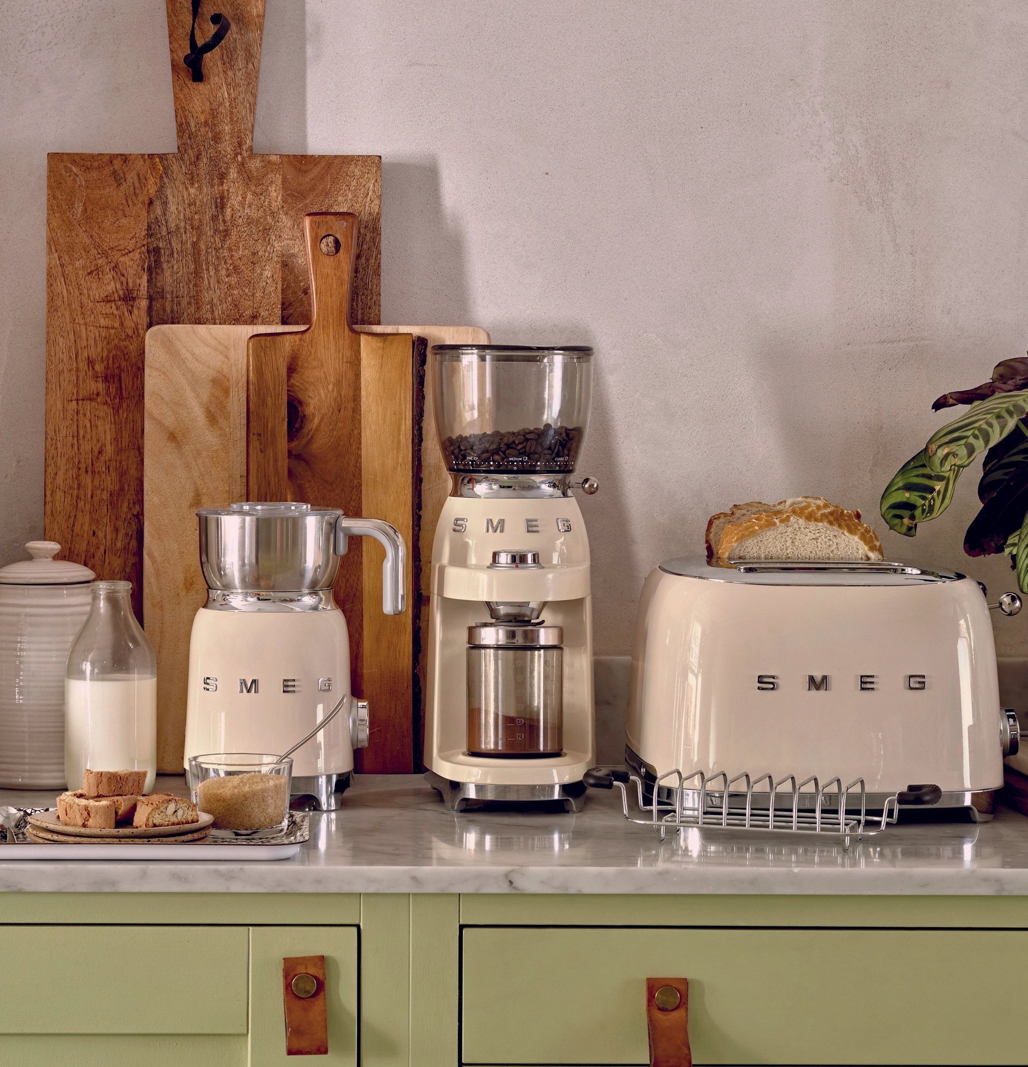 Stilren kjøkkenbenk med kremfargede SMEG-kjøkkenapparater, skjærefjøler og brødskiver i en lys, moderne innredning.