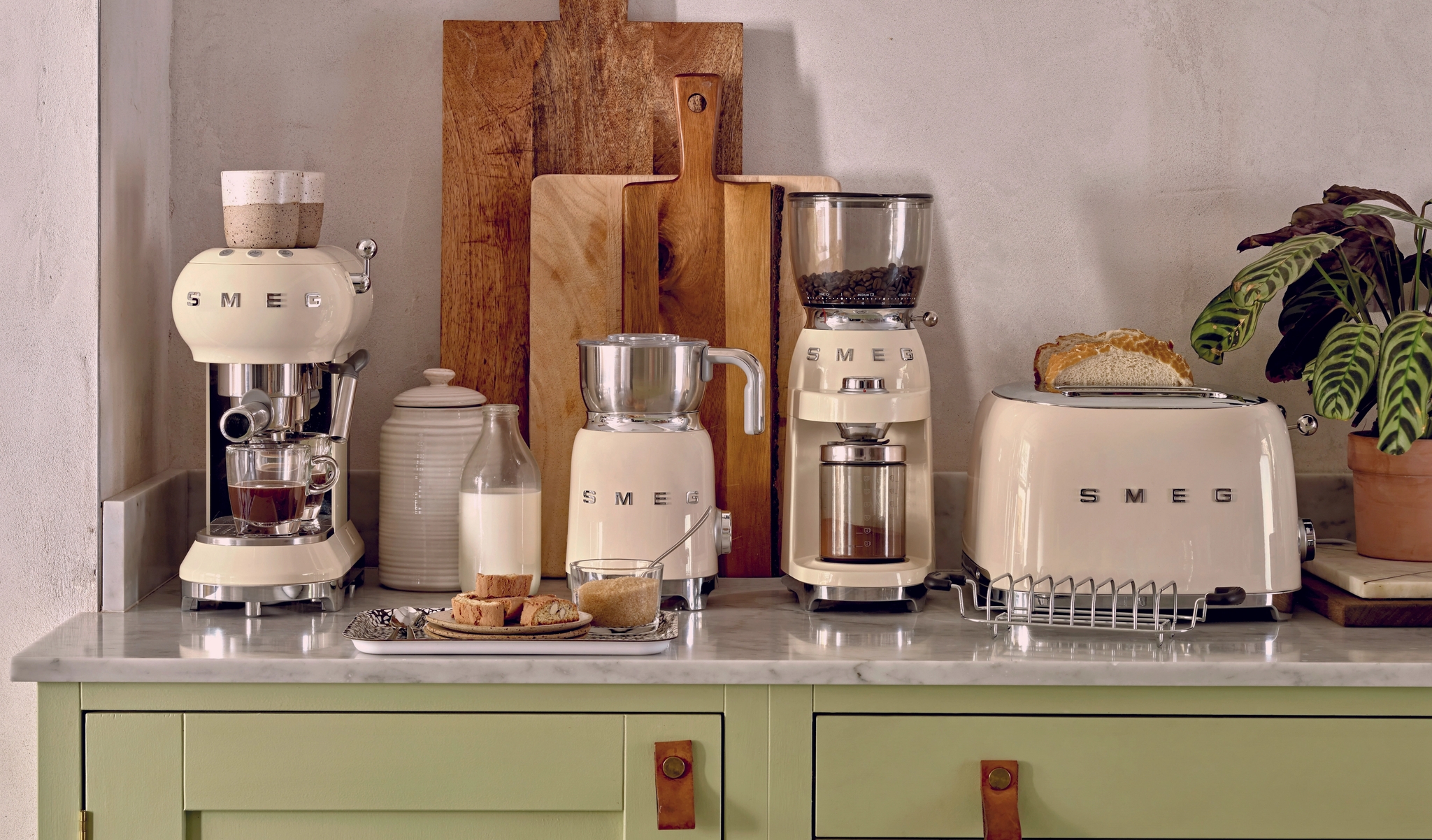 Stilren kjøkkenbenk med kremfargede SMEG-kjøkkenapparater, skjærefjøler og brødskiver i en lys, moderne innredning.