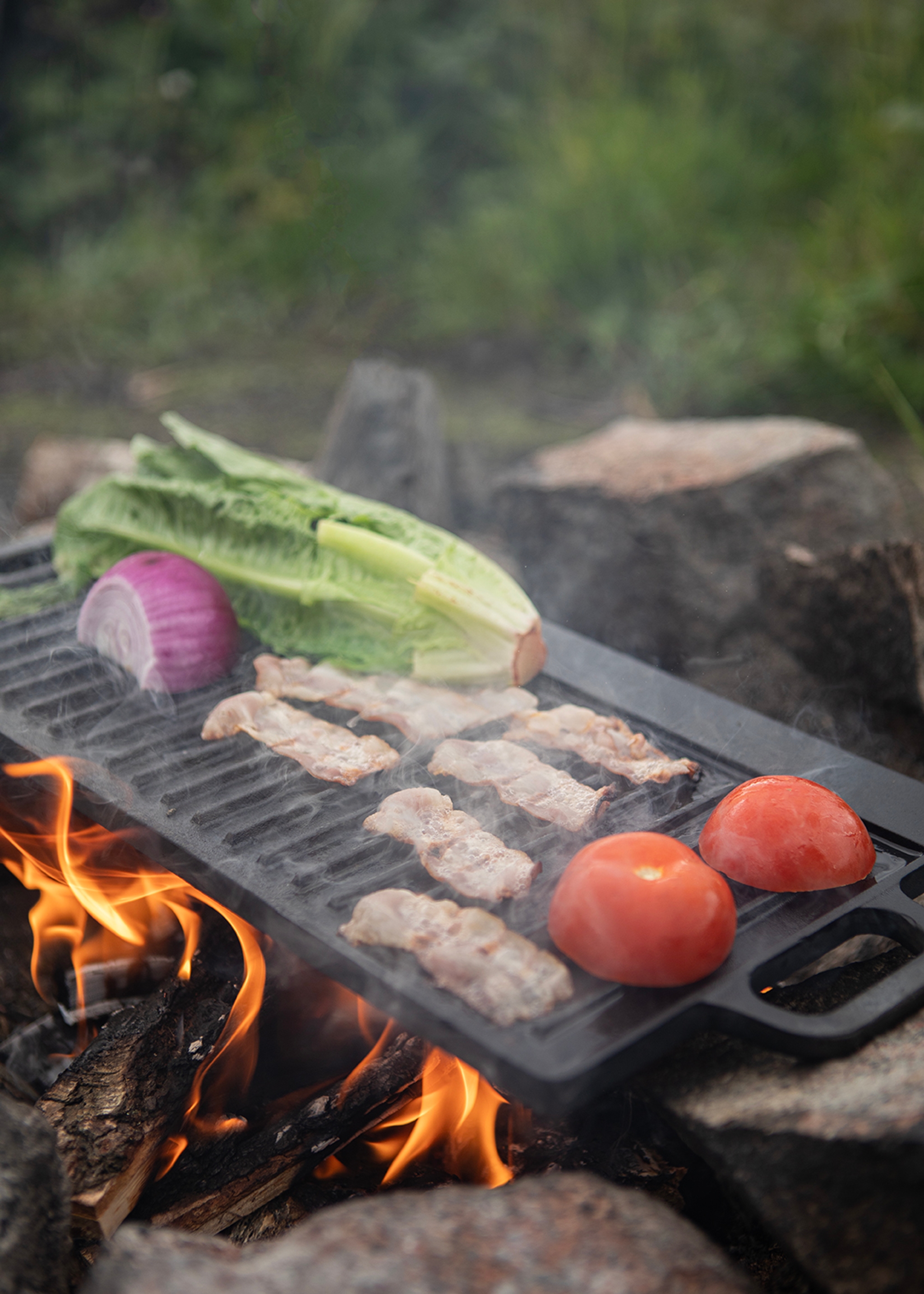 Bacon, tomater, rödlök och romansallad grillas över öppen eld utomhus.